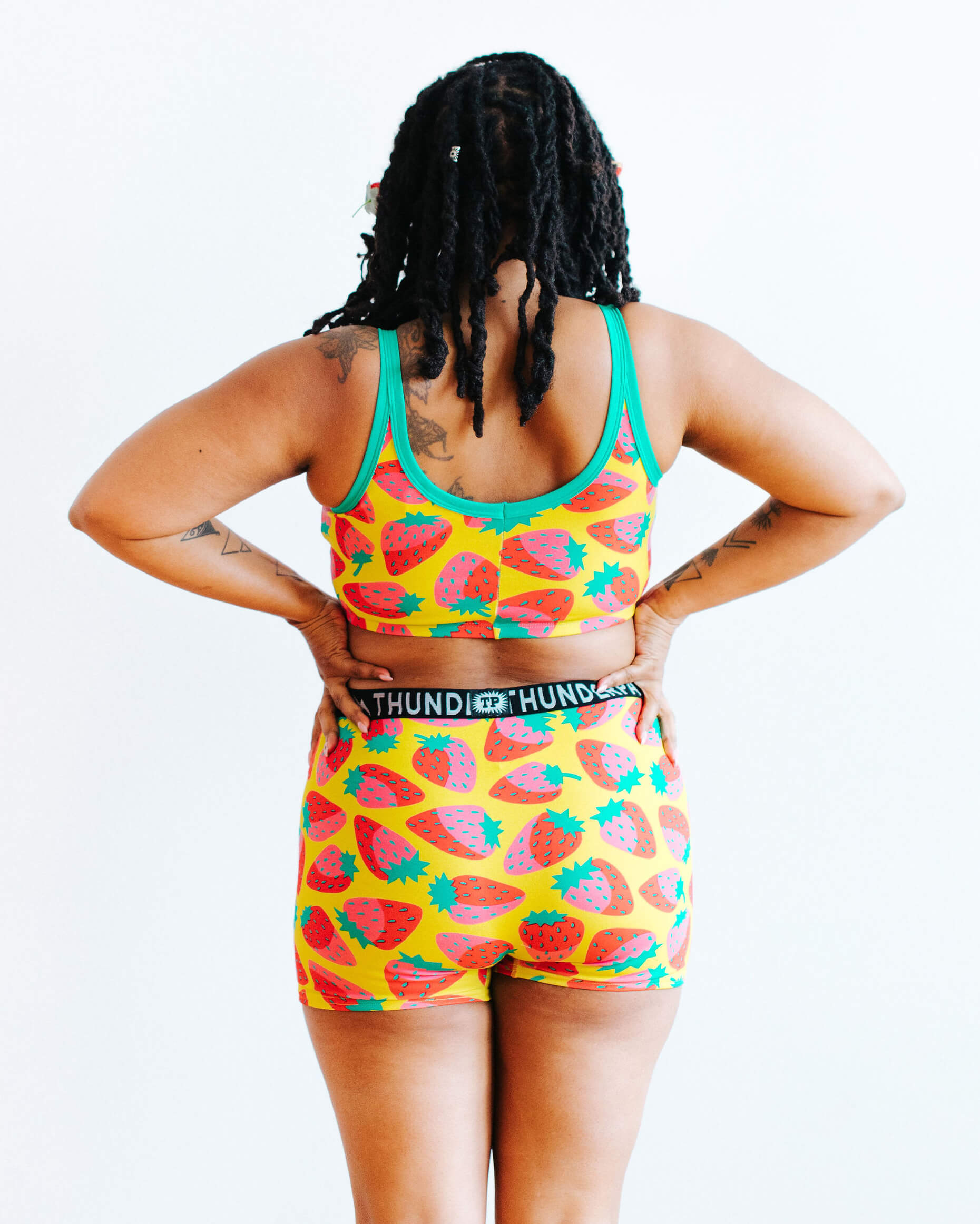 Model wearing Thunderpants Longline Bra and Boxer Brief style underwear in a Strawberry print - pink, red, and peacock green on chartreuse. 