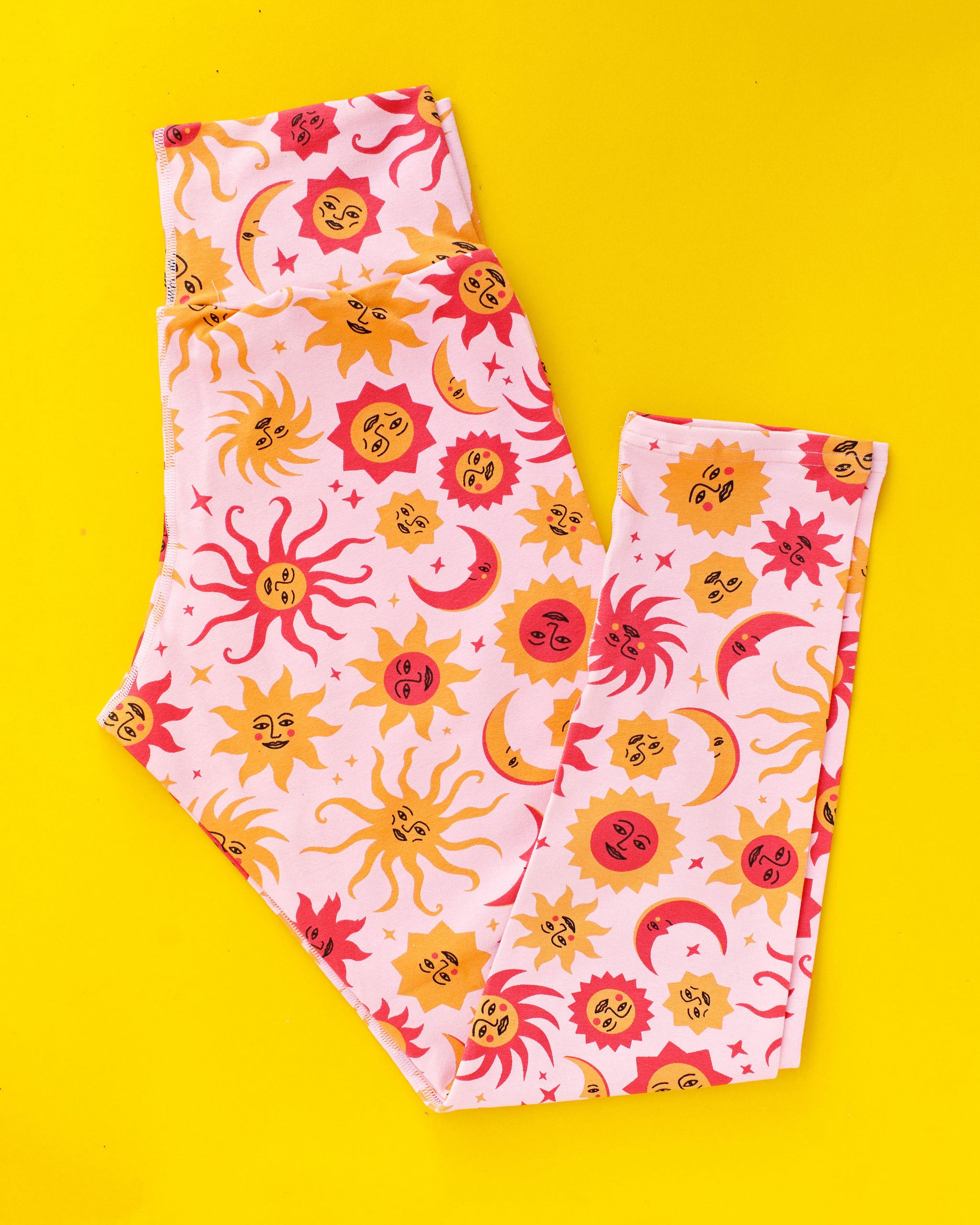 Flat lay of Thunderpants Ankle Length Leggings in Luna y Sol - moons and suns in pinks and orange.