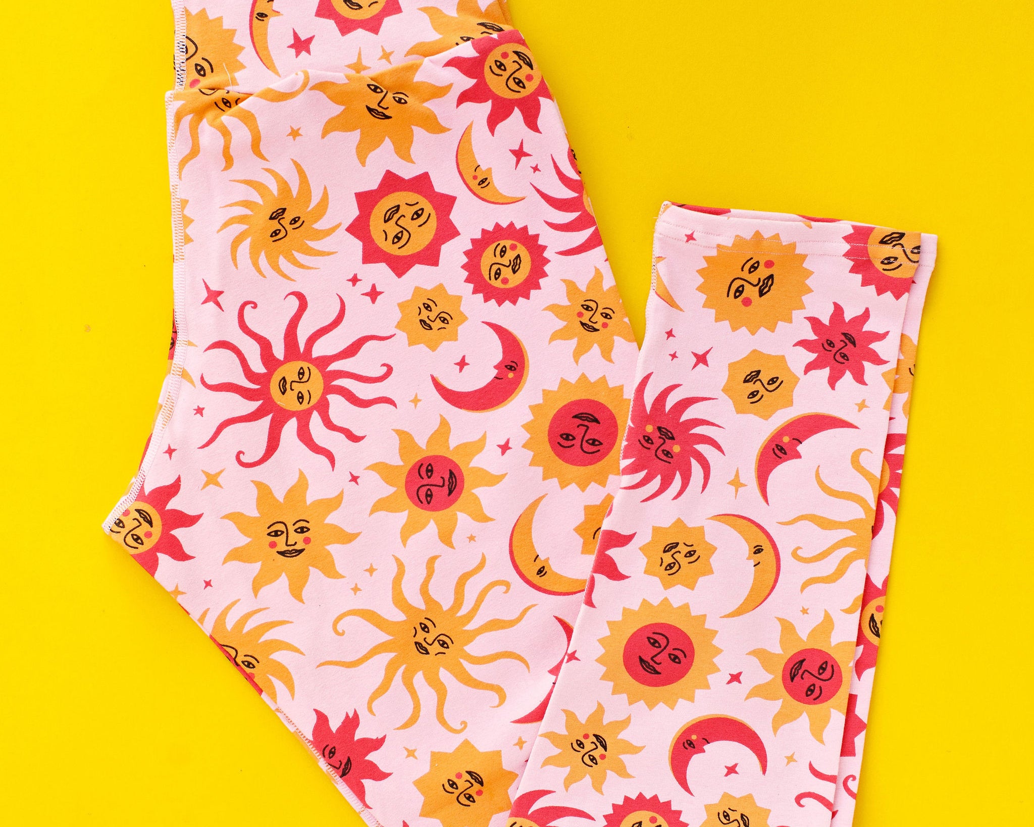 Flat lay of Thunderpants Ankle Length Leggings in Luna y Sol - moons and suns in pinks and orange.