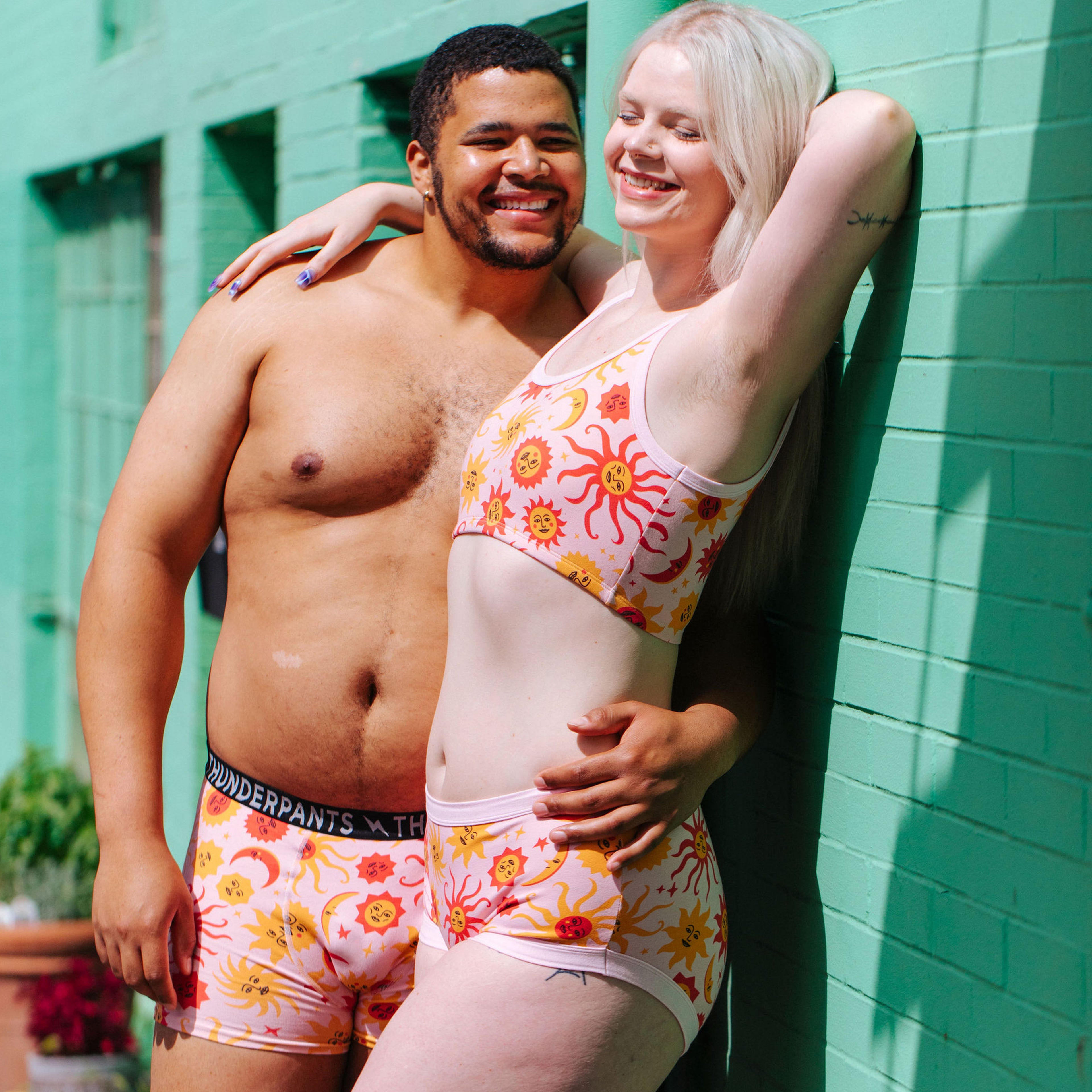 Two models wearing various Thunderpants items in Luna y Sol print - pink, yellow, and orange suns and moons.