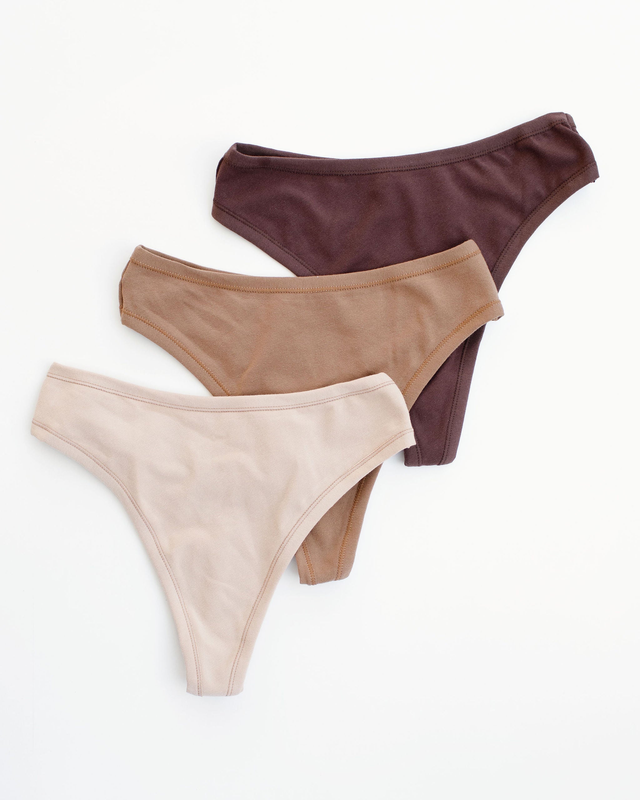 Flat lay of Thunderpants Thong style underwear in Pine Nut (a tan), Hazelnut (a light-brown), and Chestnut (a dark brown). 
