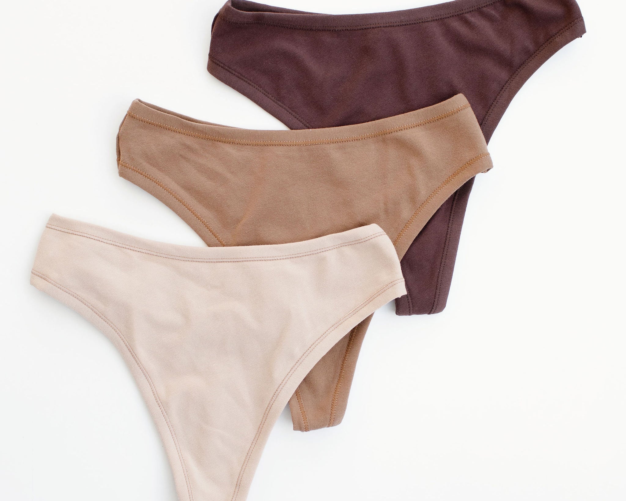 Flay lay of Thunderpants Thong style underwear in Pine Nut (a tan), Hazelnut (a light brown), and Chestnut (a dark brown).