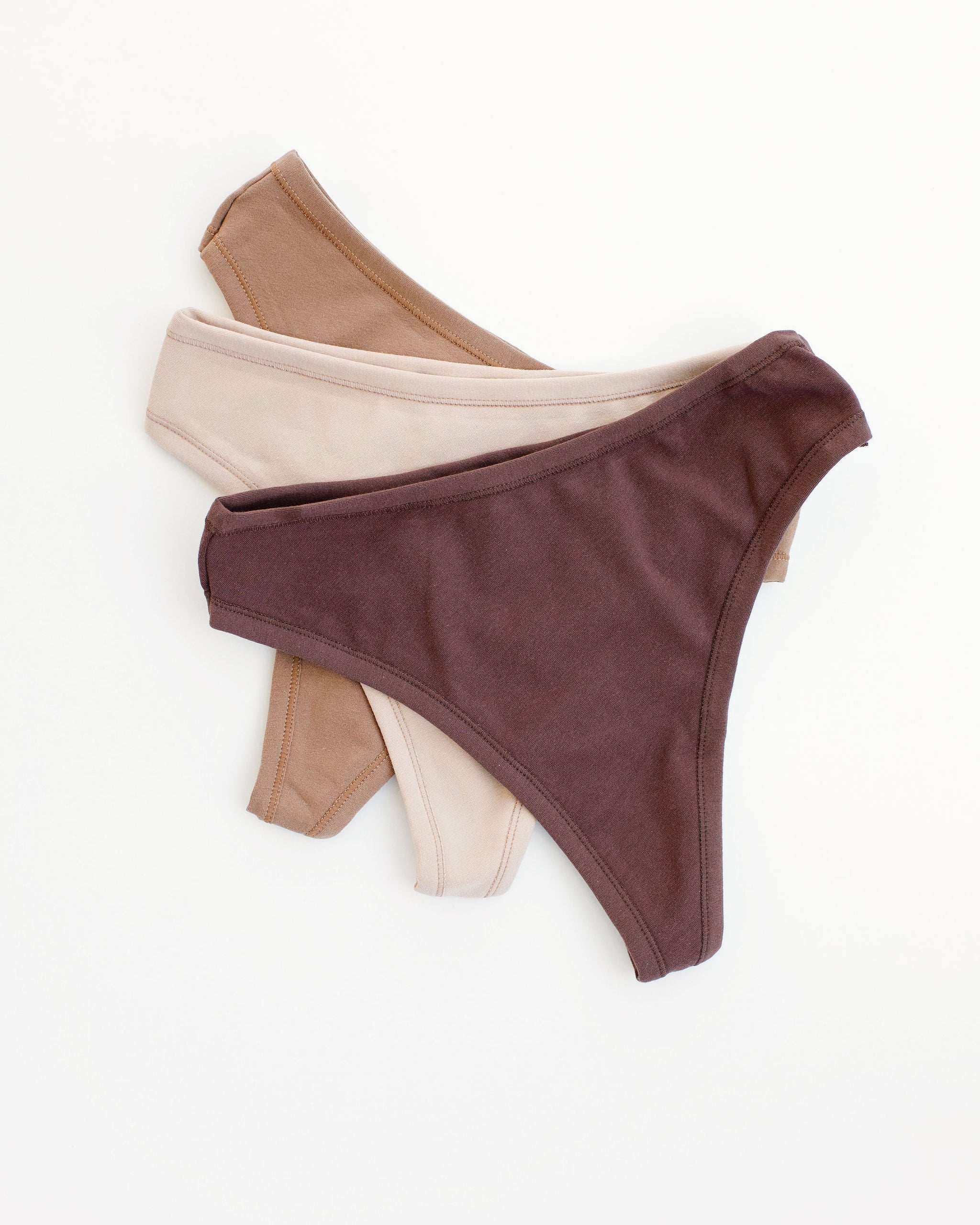 Flay lay of Thunderpants Thong style underwear in Chestnut (a dark brown), Hazelnut (a light brown), and Pine Nut (a tan).