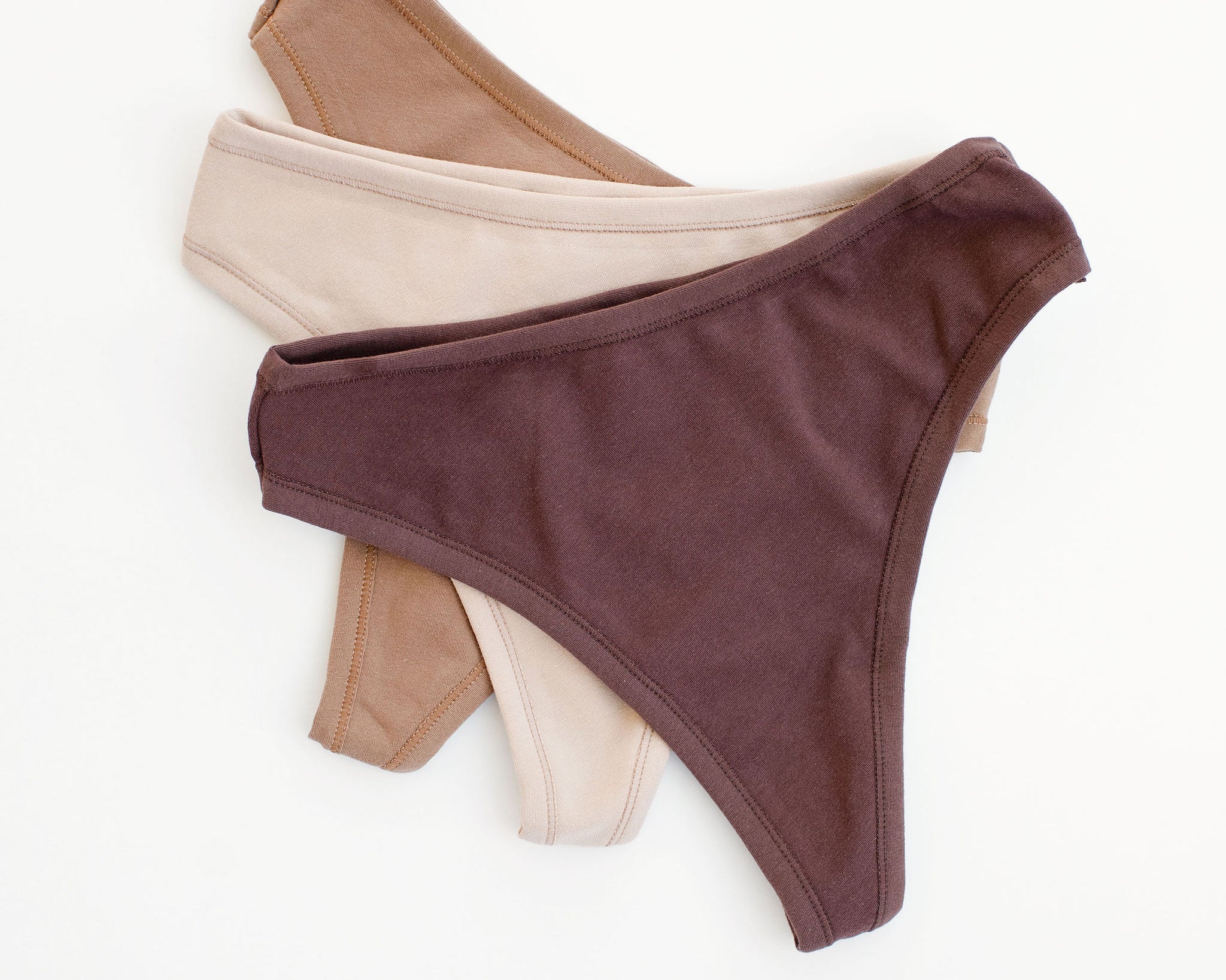 Flay lay of Thunderpants Thong style underwear in Chestnut (a dark brown), Hazelnut (a light brown), and Pine Nut (a tan).