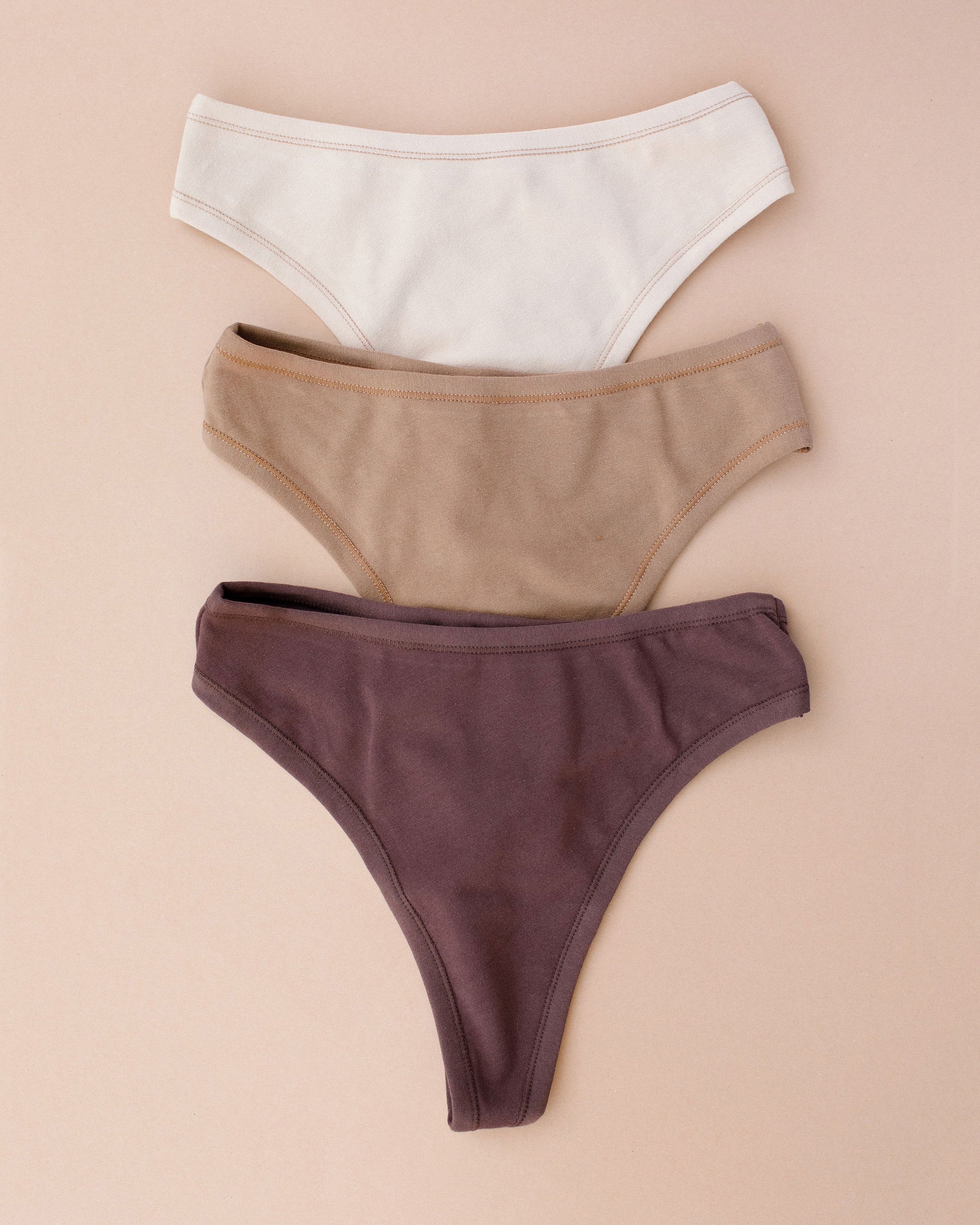 Flay lay of Thunderpants Thong style underwear in Chestnut (a dark brown), Hazelnut (a light brown), and Pine Nut (a tan).
