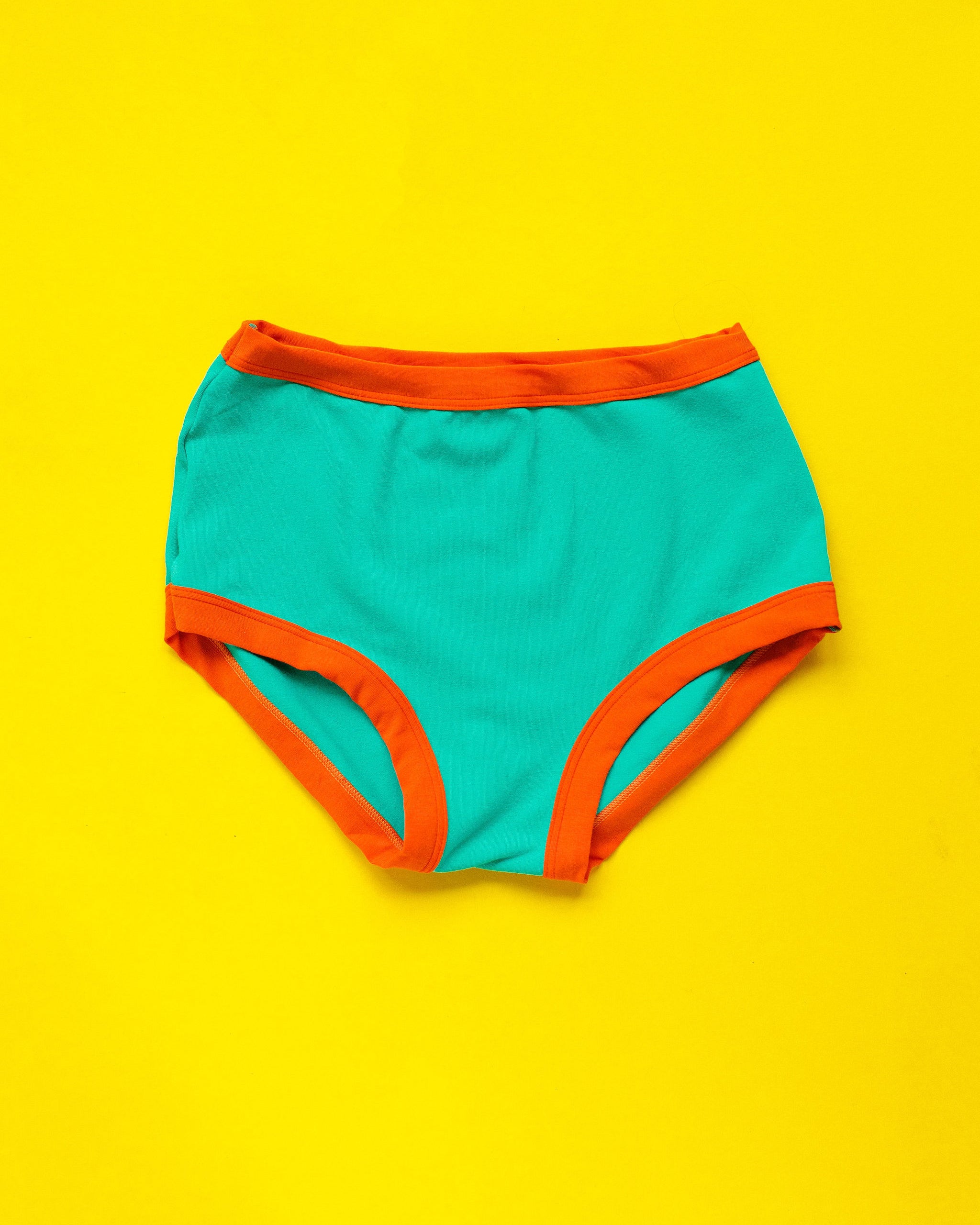 Flat lay of Thunderpants Original style underwear in Bird in Paradise - peacock green with orange binding.