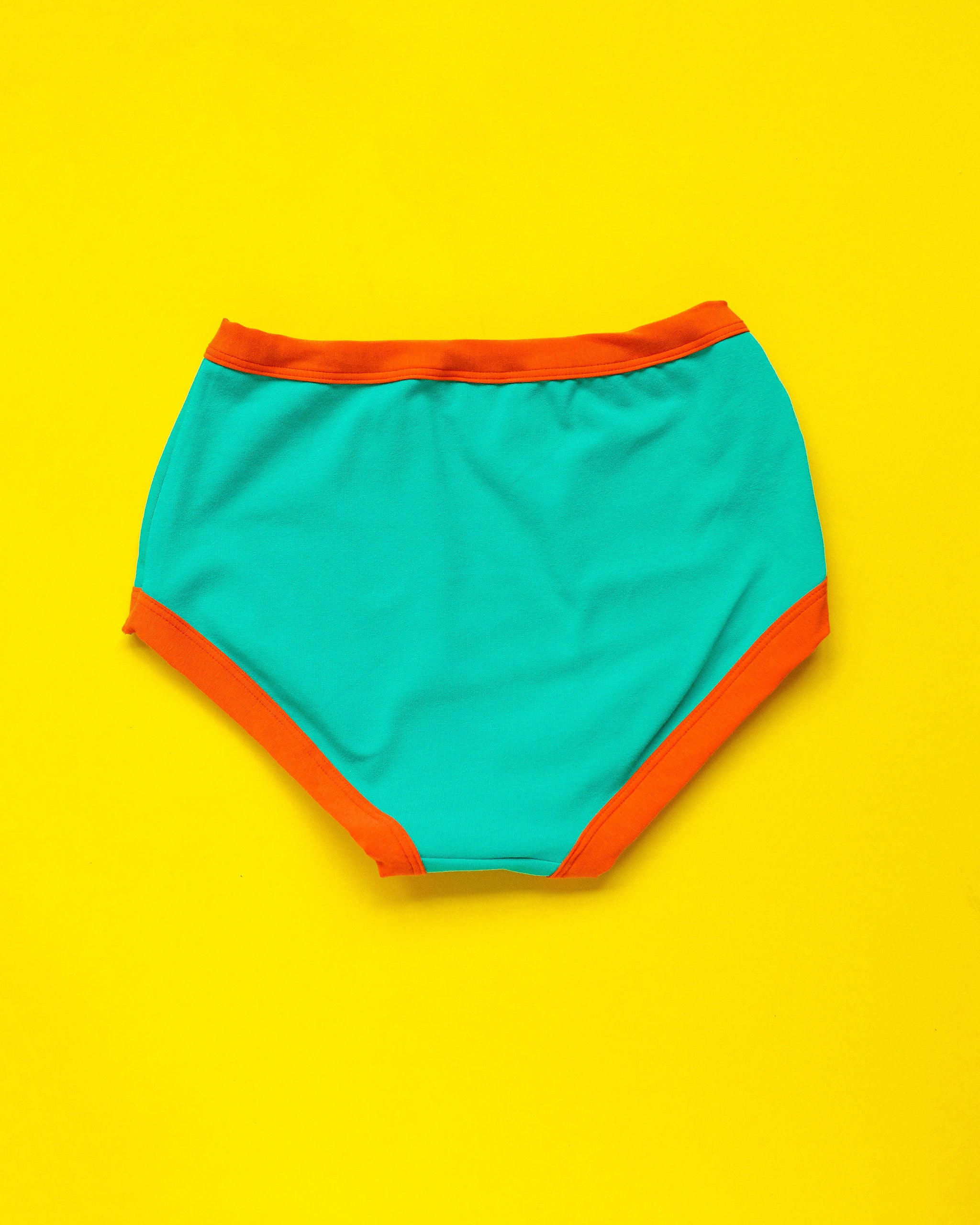 Flat lay of Thunderpants Original style underwear in Bird in Paradise - peacock green with orange binding.
