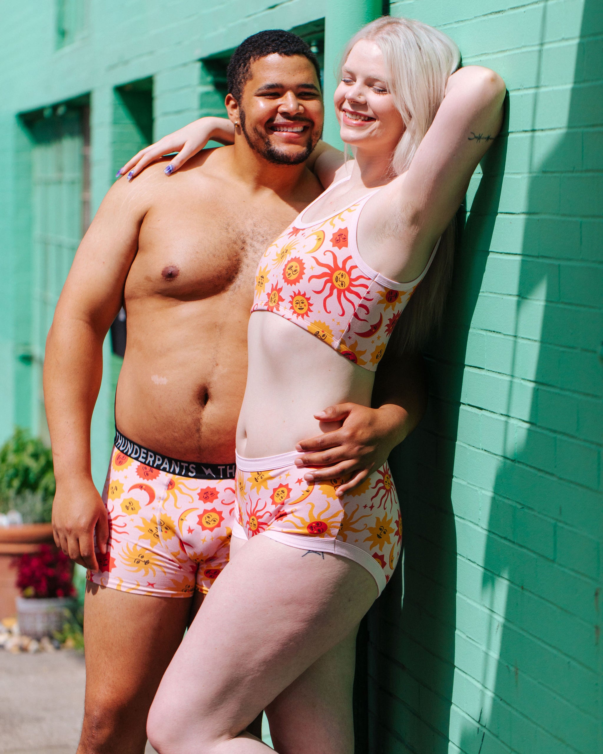 Two models wearing Thunderpants Original style underwear, Longline Bra, and Boxer Brief style underwear in Luna Y Sol print - pink, yellow, and orange suns and moons.