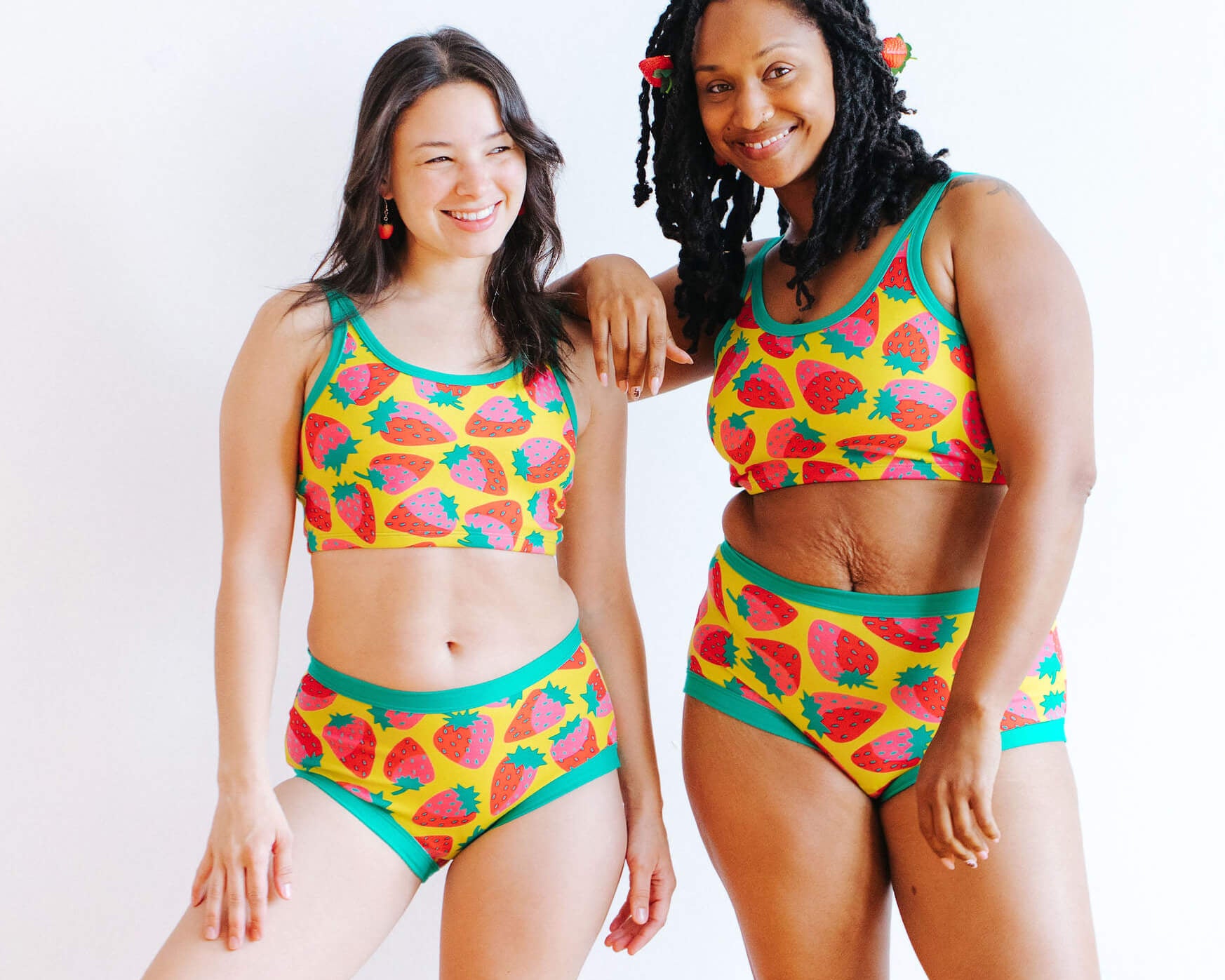 Models wearing Thunderpants Original style underwear and Longline Bra in a Strawberry print - pink, red, and peacock green on chartreuse. 