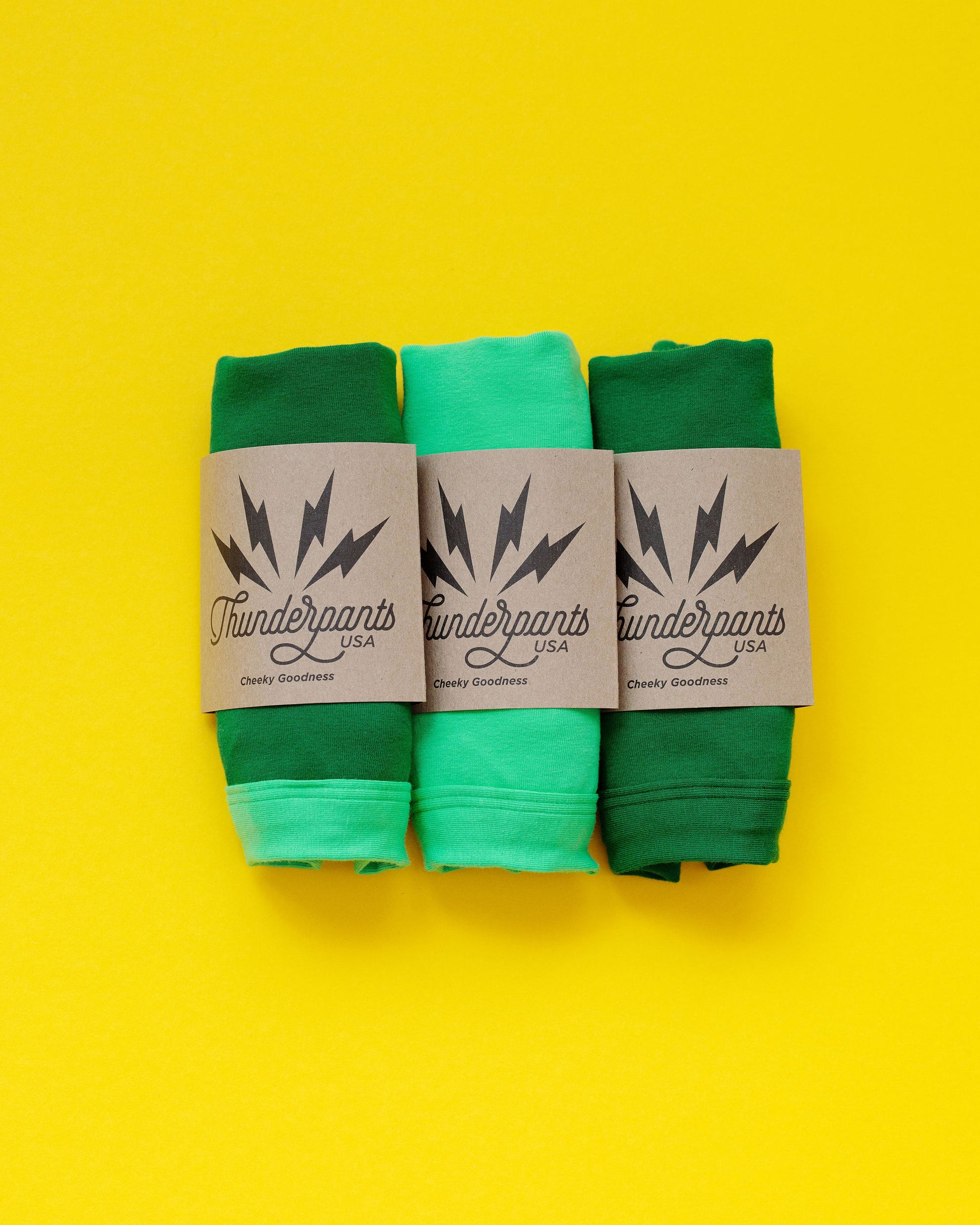 Three different green colored packaged underwear on a yellow background.