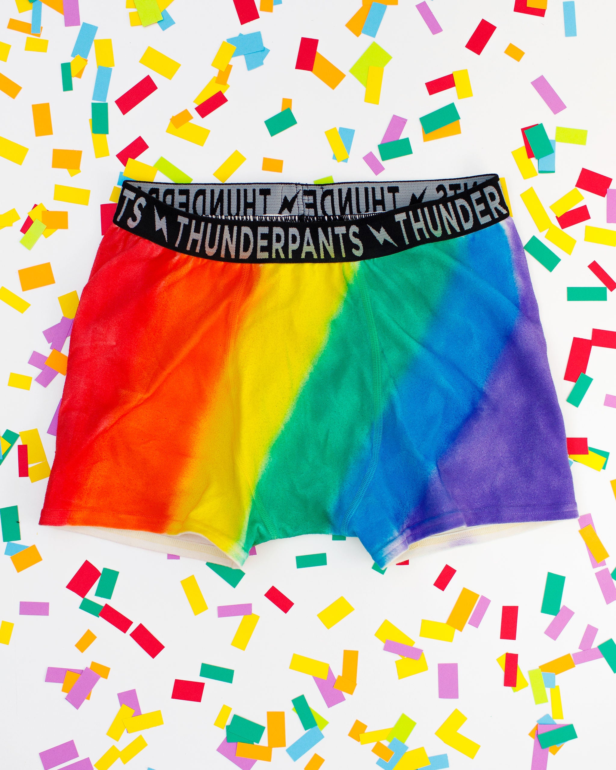 Thunderpants organic cotton Boxer Brief style underwear in hand painted rainbow stripes for Pride laying on rainbow confetti.