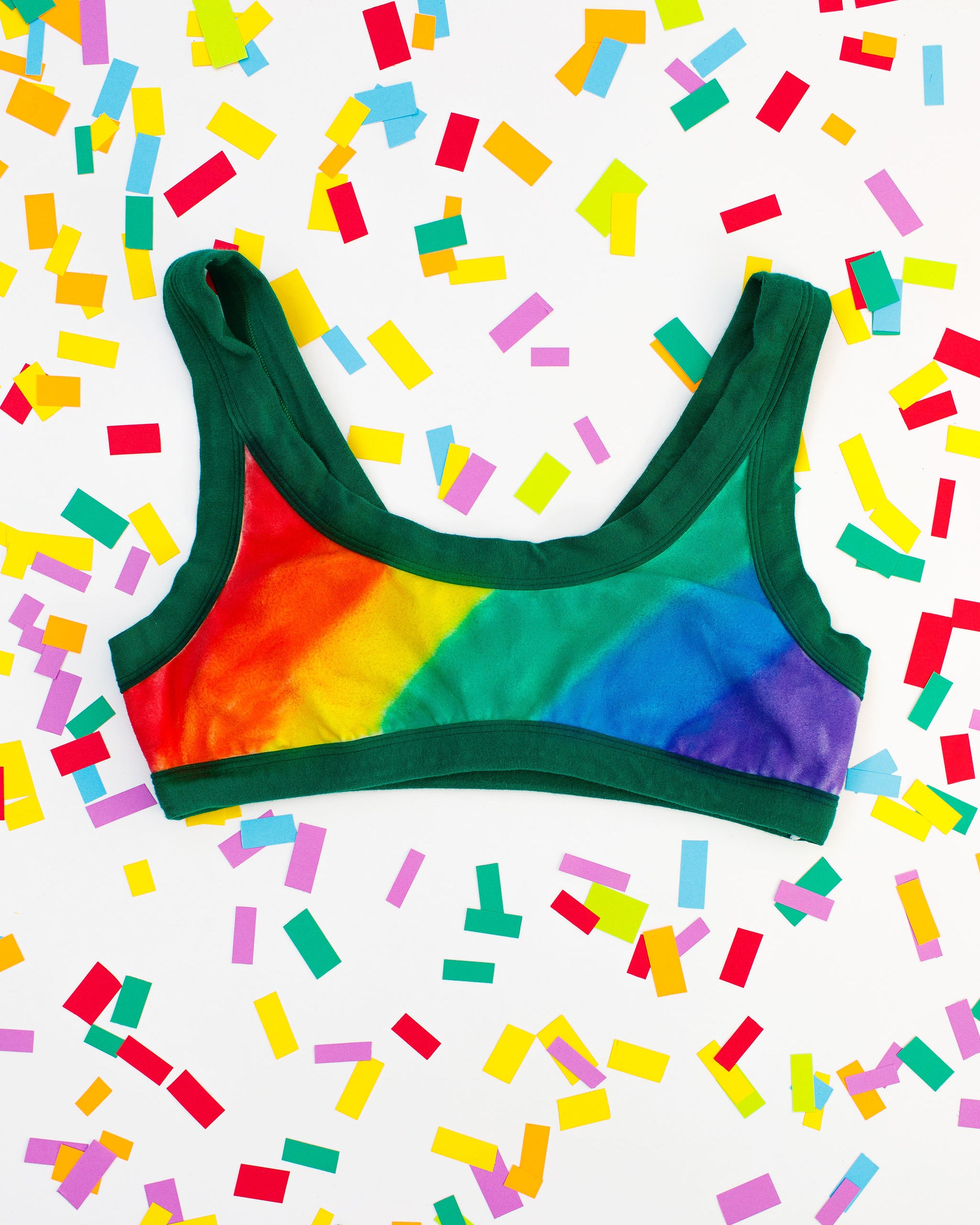 Flat lay of Thunderpants organic cotton Bralette in hand painted rainbow stripes for Pride laying on confetti.