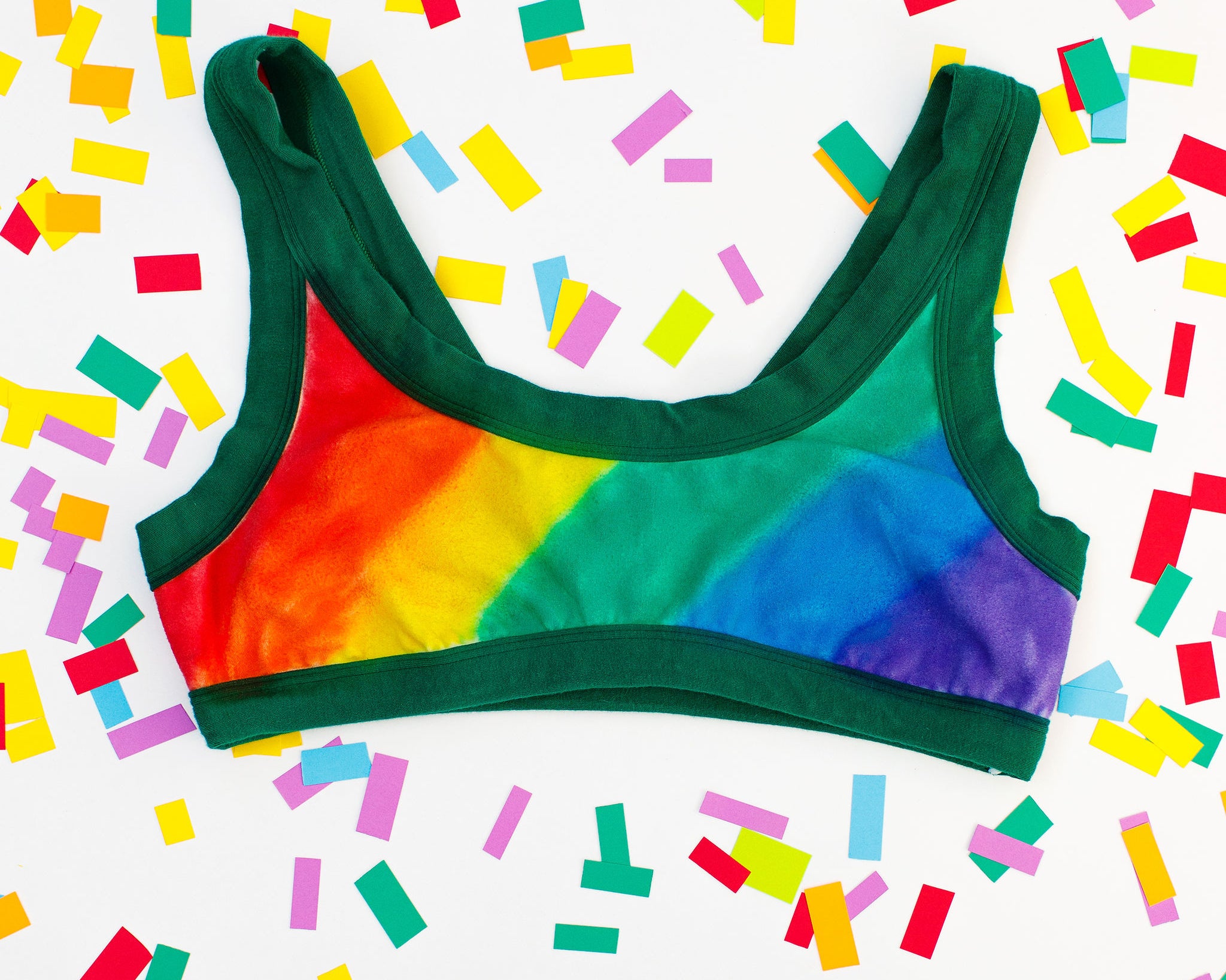 Flat lay of Thunderpants organic cotton Bralette in hand painted rainbow stripes for Pride laying on confetti.