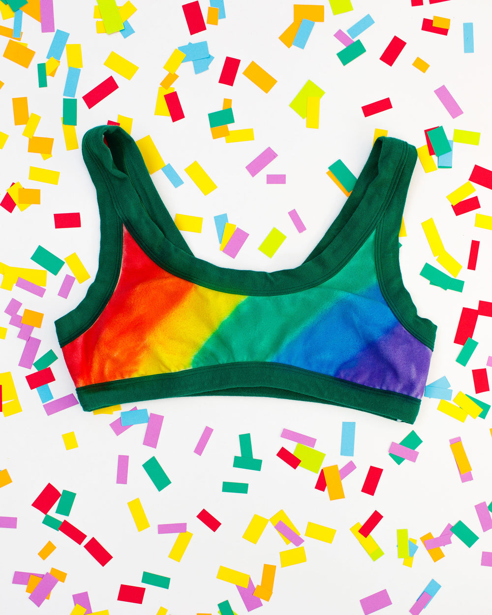 Flat lay of Thunderpants organic cotton Bralette in hand painted rainbow stripes for Pride laying on confetti.