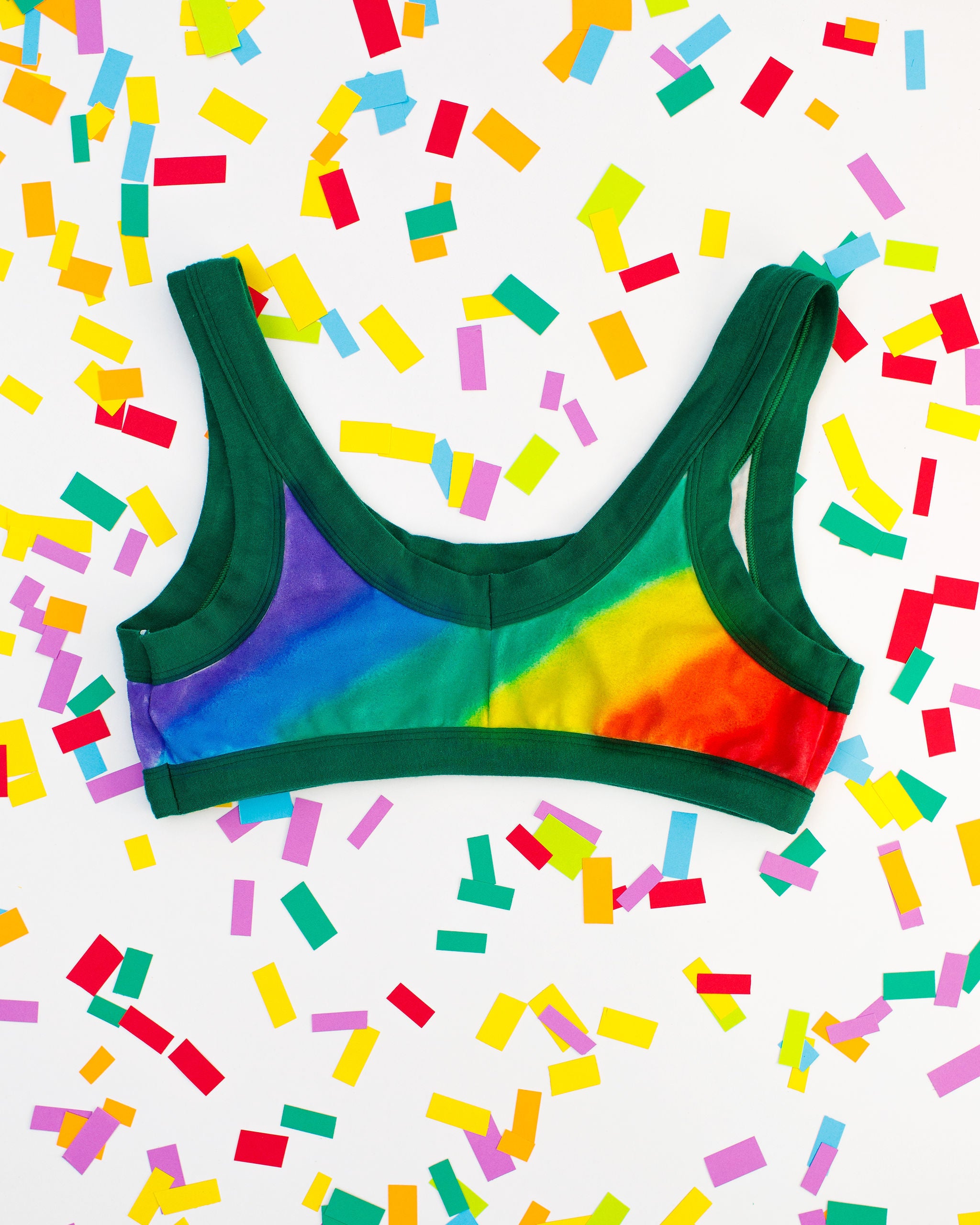 Flat lay of Thunderpants organic cotton Bralette in hand painted rainbow stripes for Pride laying on confetti.