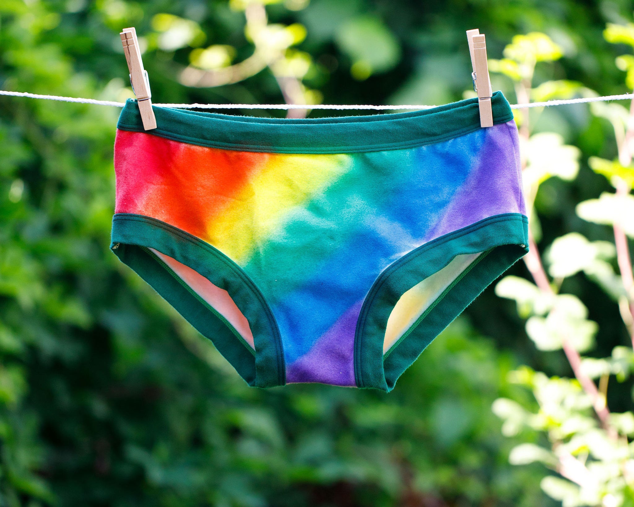 Thunderpants organic cotton Hipster style underwear in hand painted rainbow stripes for Pride hanging on a clothes line in greenery. 