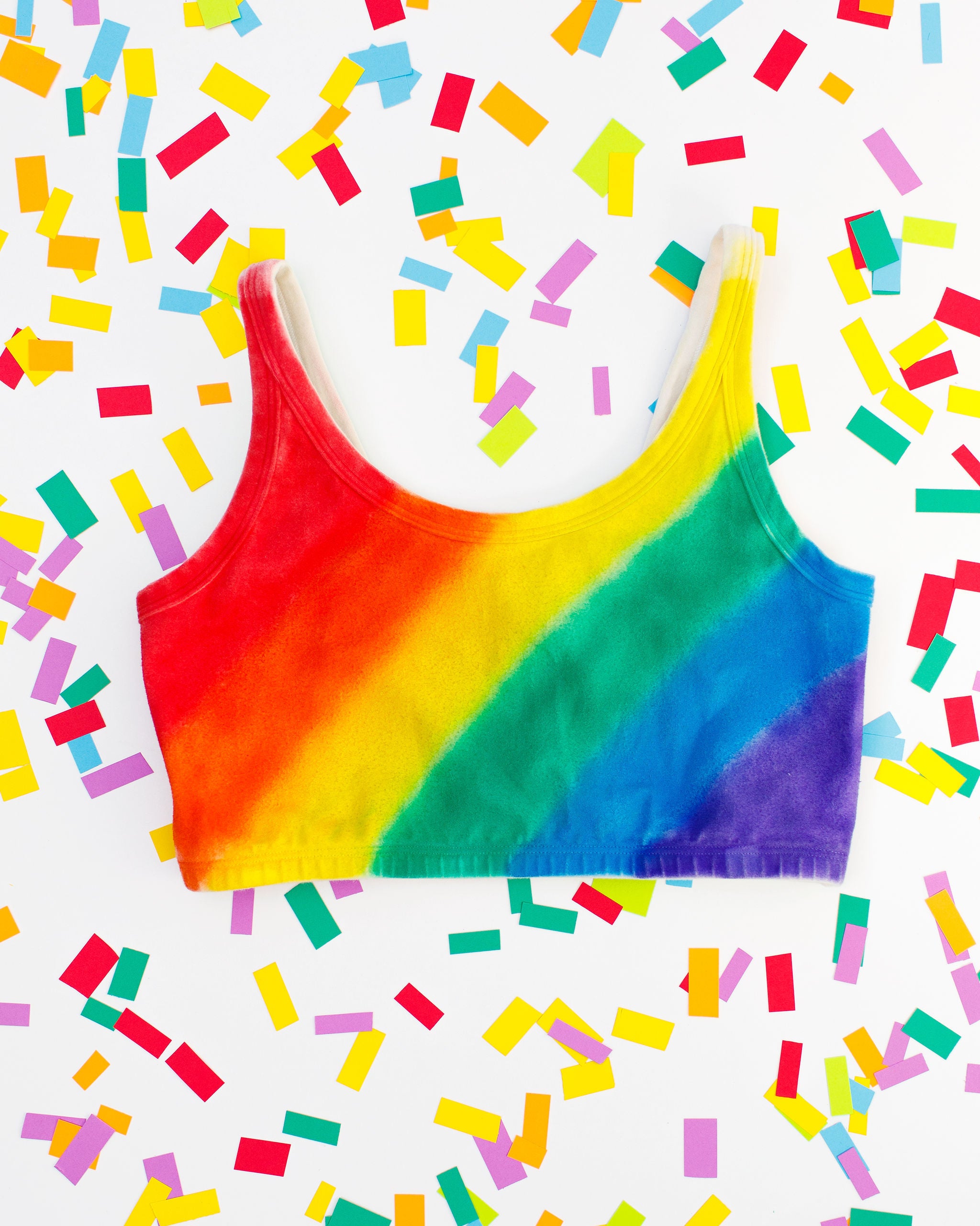 Thunderpants organic cotton Longline Bra in hand painted rainbow stripes for Pride laying on rainbow confetti. 