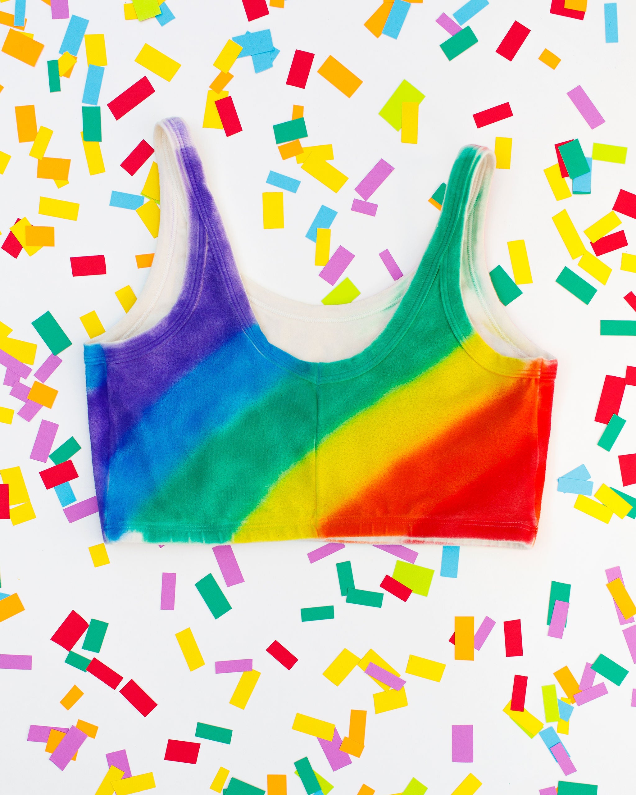 Thunderpants organic cotton Longline Bra in hand painted rainbow stripes for Pride laying on rainbow confetti. 