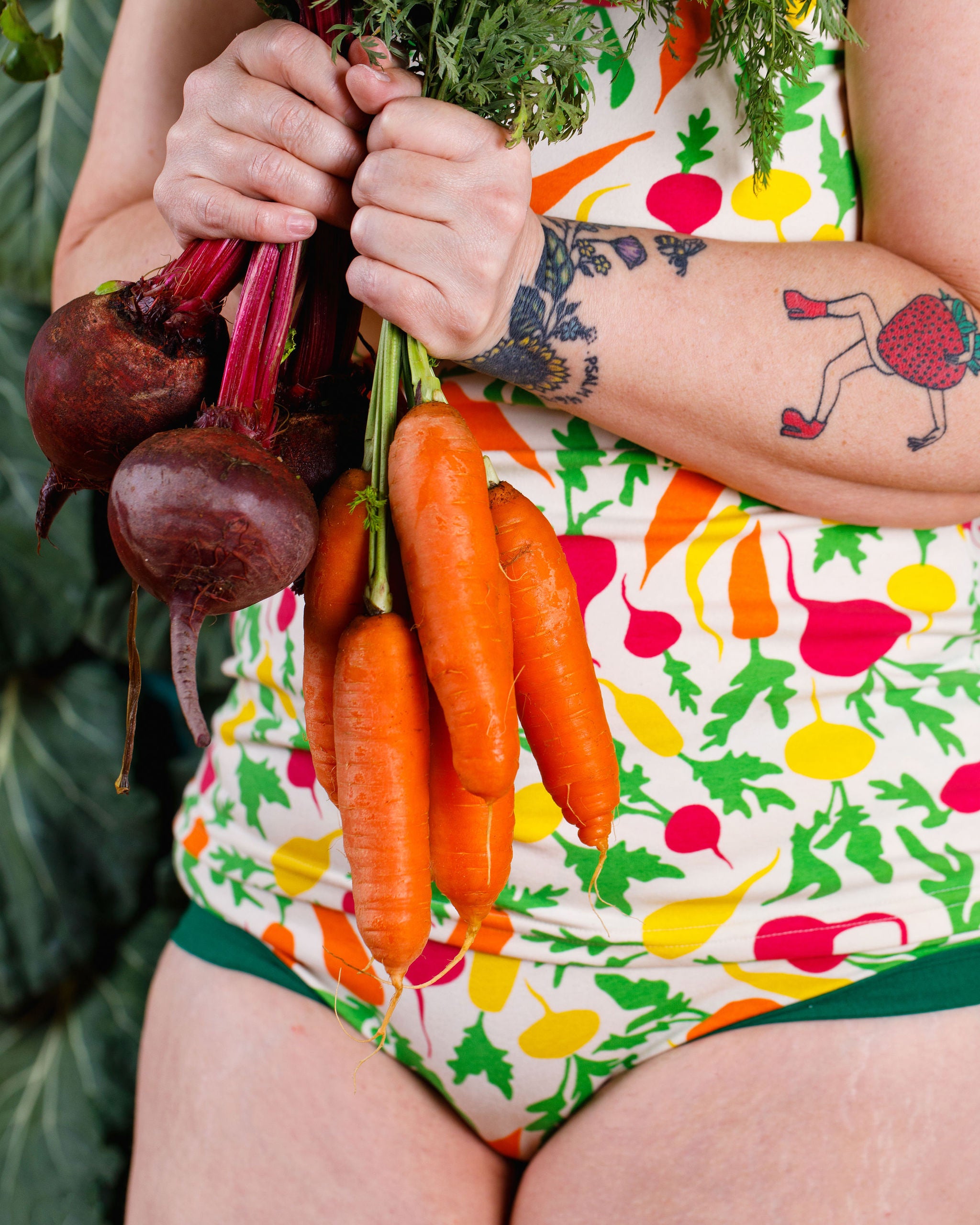 Close up of model holding beets and carrots and wearing Thunderants Camisole and Hipster style underwear in Root Veggies print - yellow, orange, pink, and green vegetables.