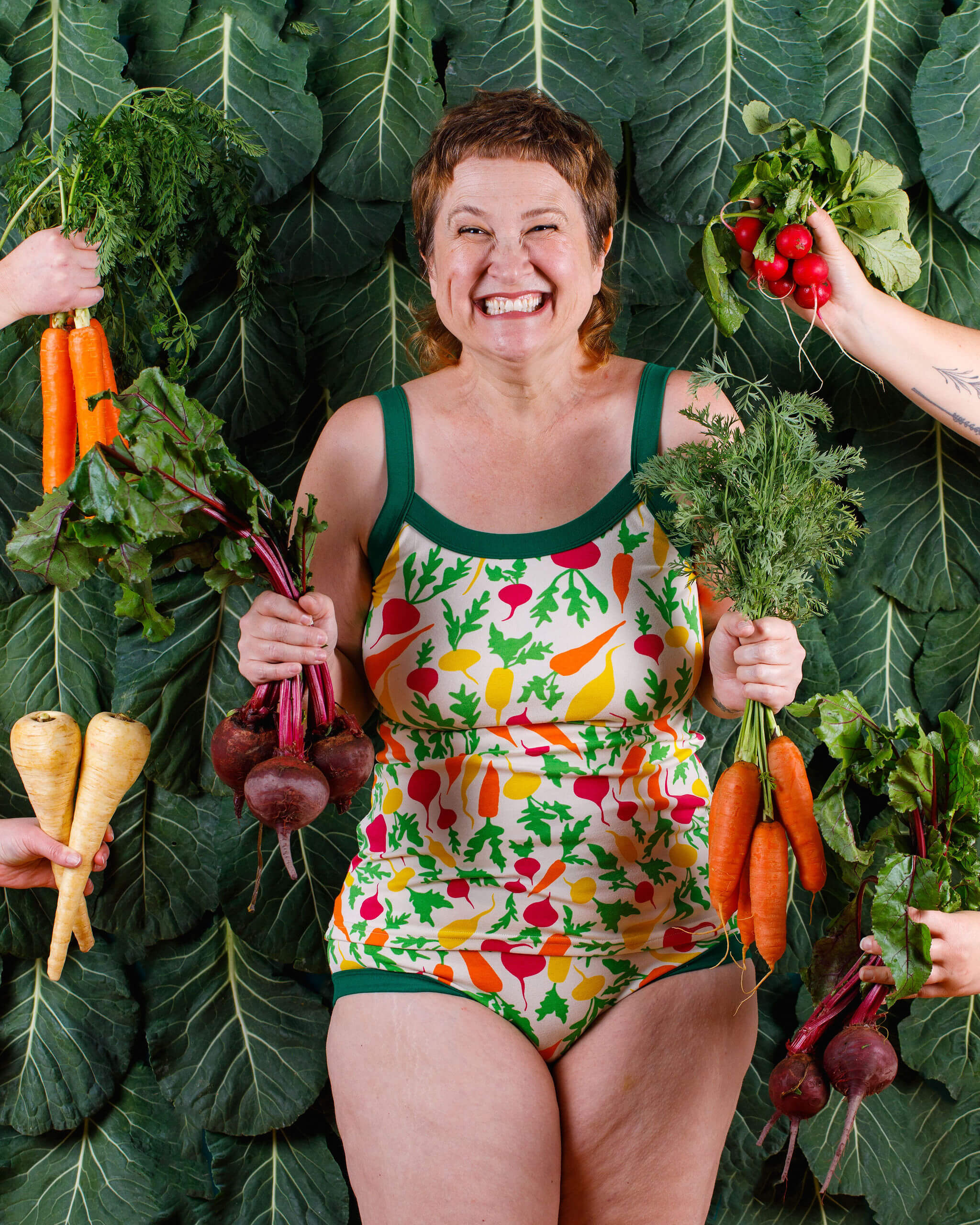 Model smiling big while wearing Thunderpants Camisole and Hipster style underwear in Root Veggies print and surrounded by root veggies.