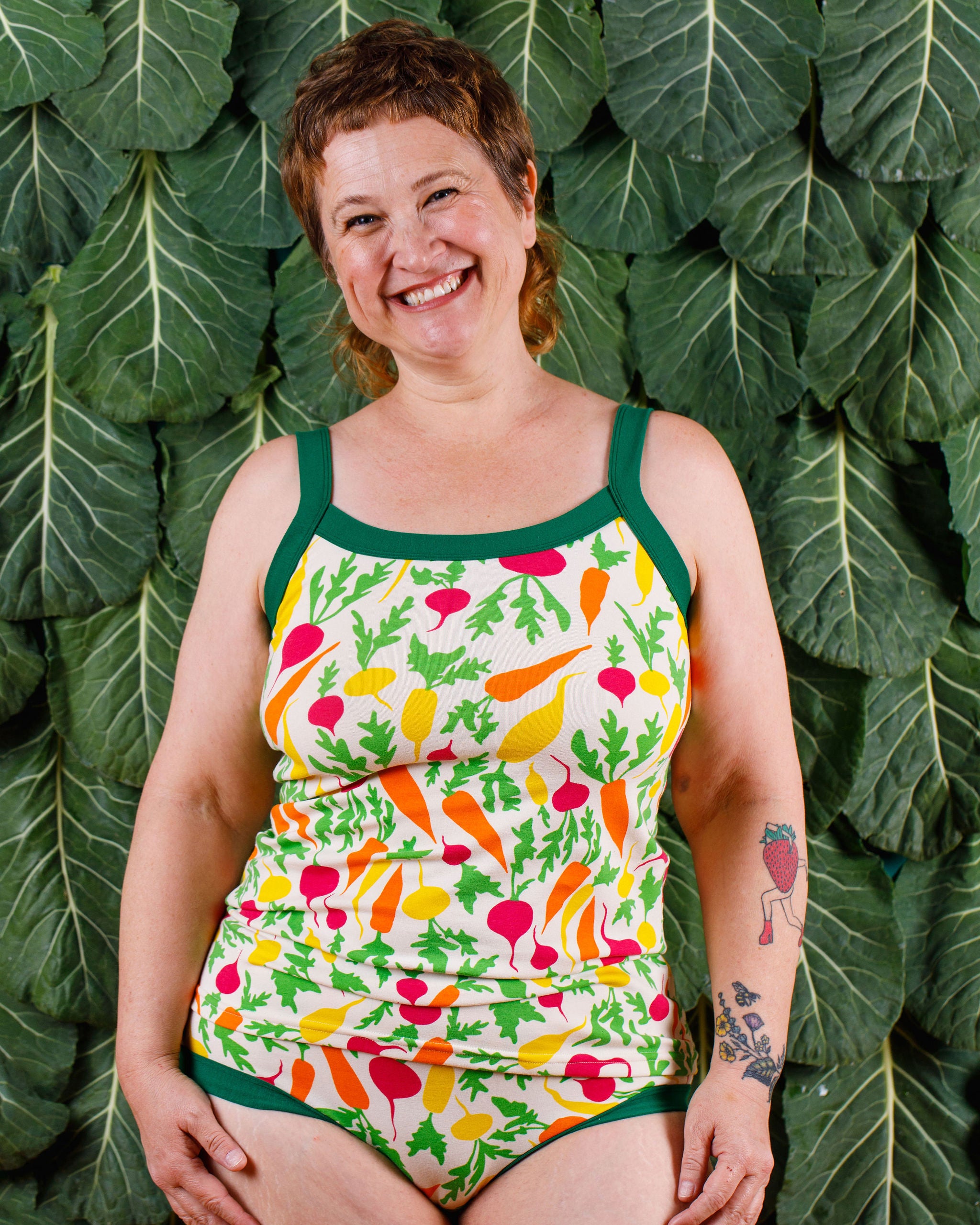 Model smiling wearing Thunderants Camisole in Root Veggies print - yellow, orange, pink, and green vegetables.