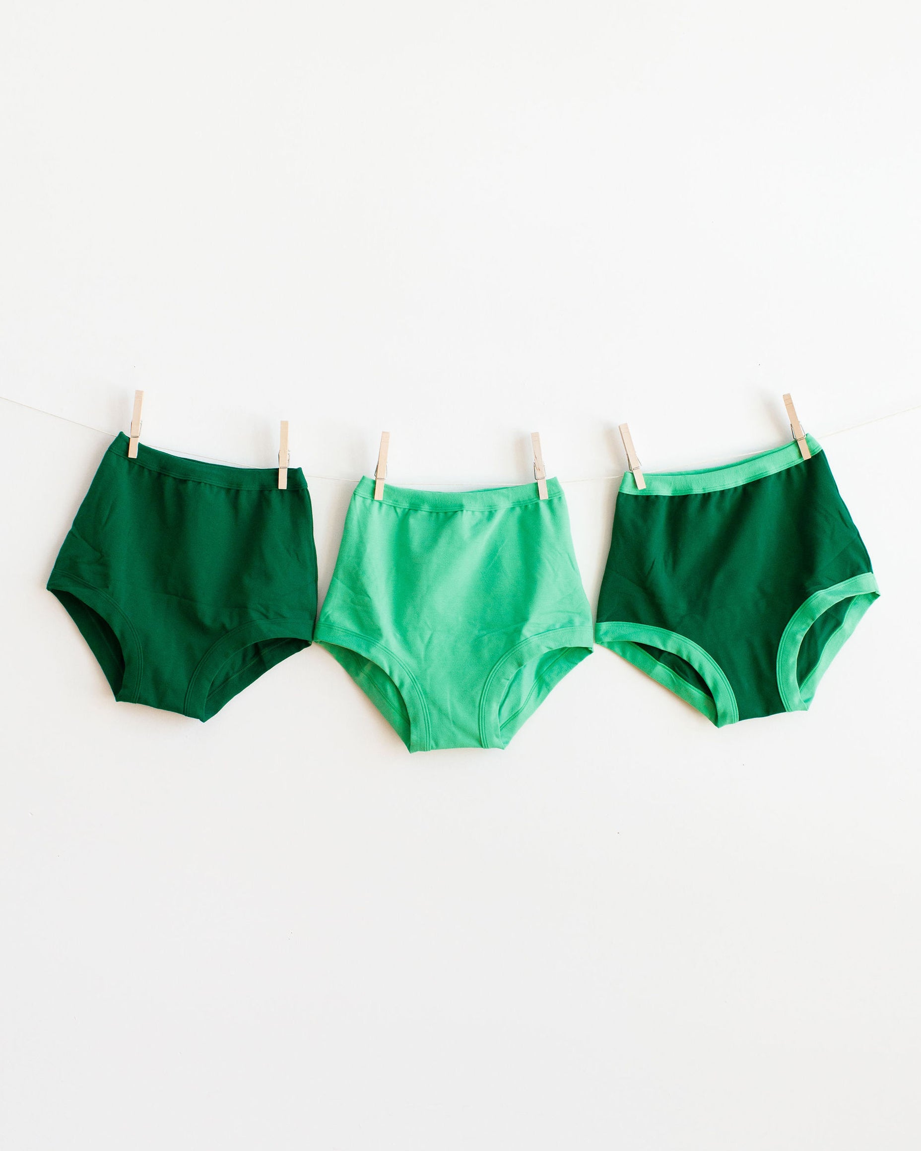 Three different green colored Sky Rise style underwear hanging on a white background.