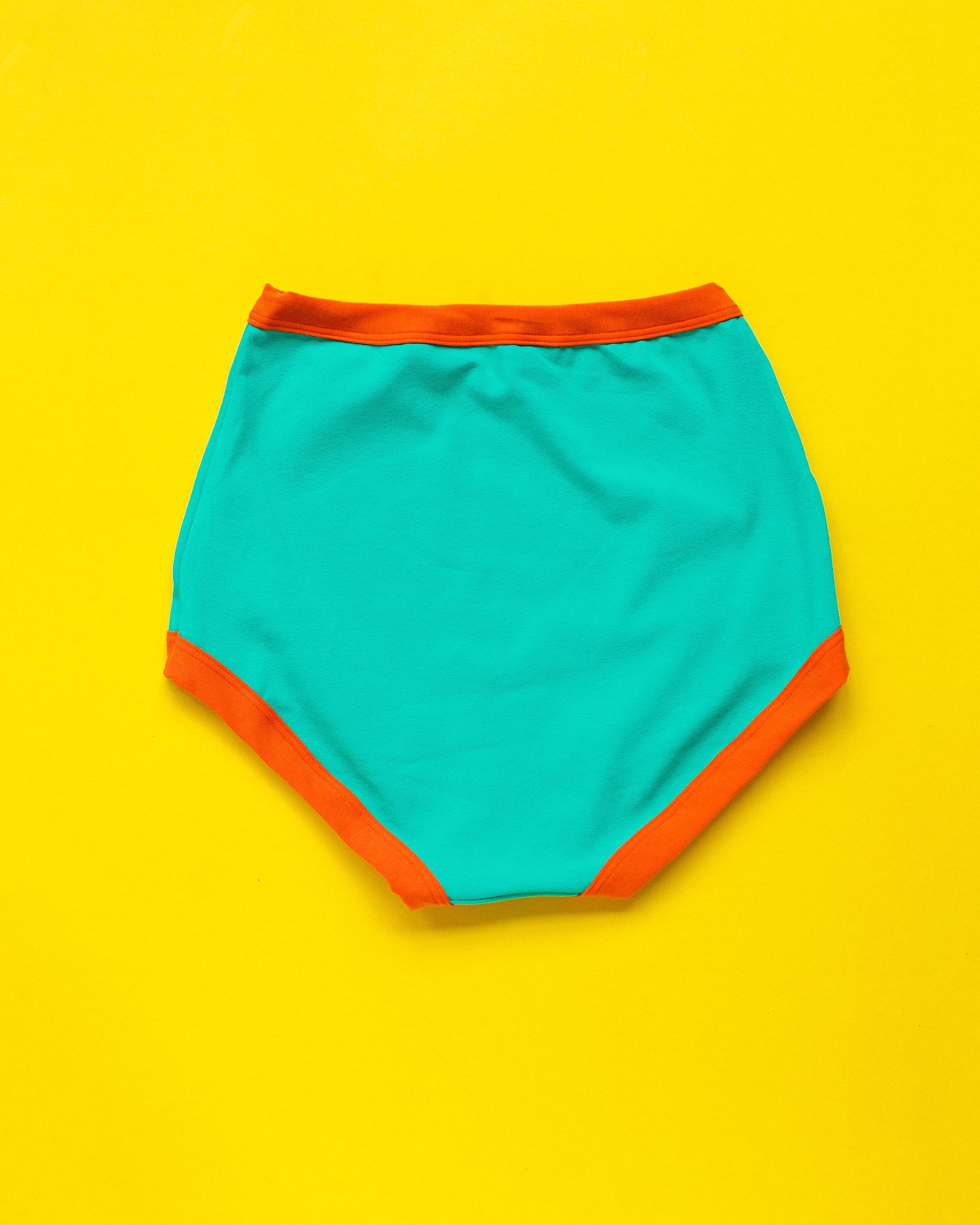 Flat lay of Thunderpants Sky Rise style underwear in Bird in Paradise - peacock green with orange binding.