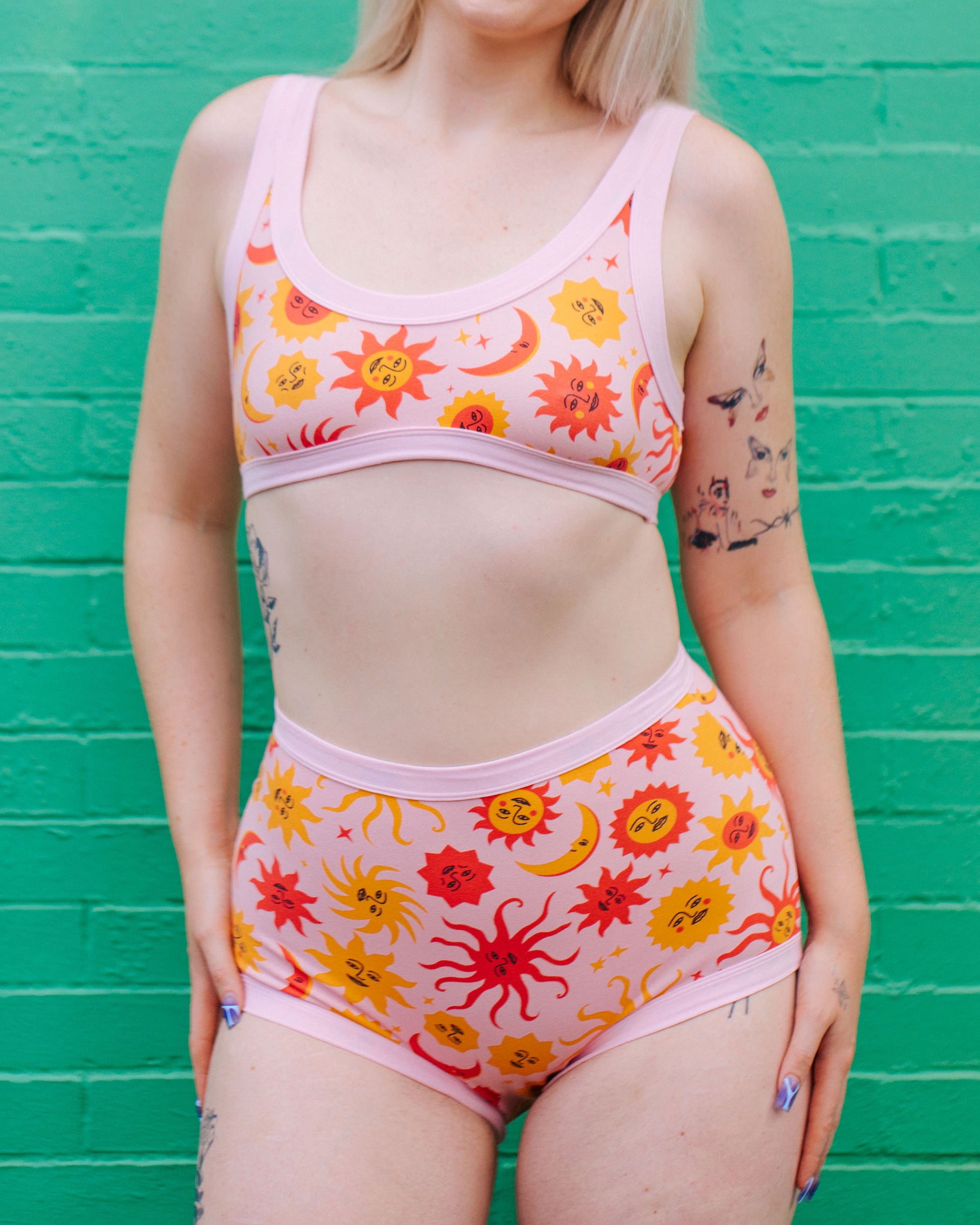 Model wearing Thunderpants Sky Rise style underwear and Bralette in Luna y Sol print - pink, yellow, and orange suns and moons.