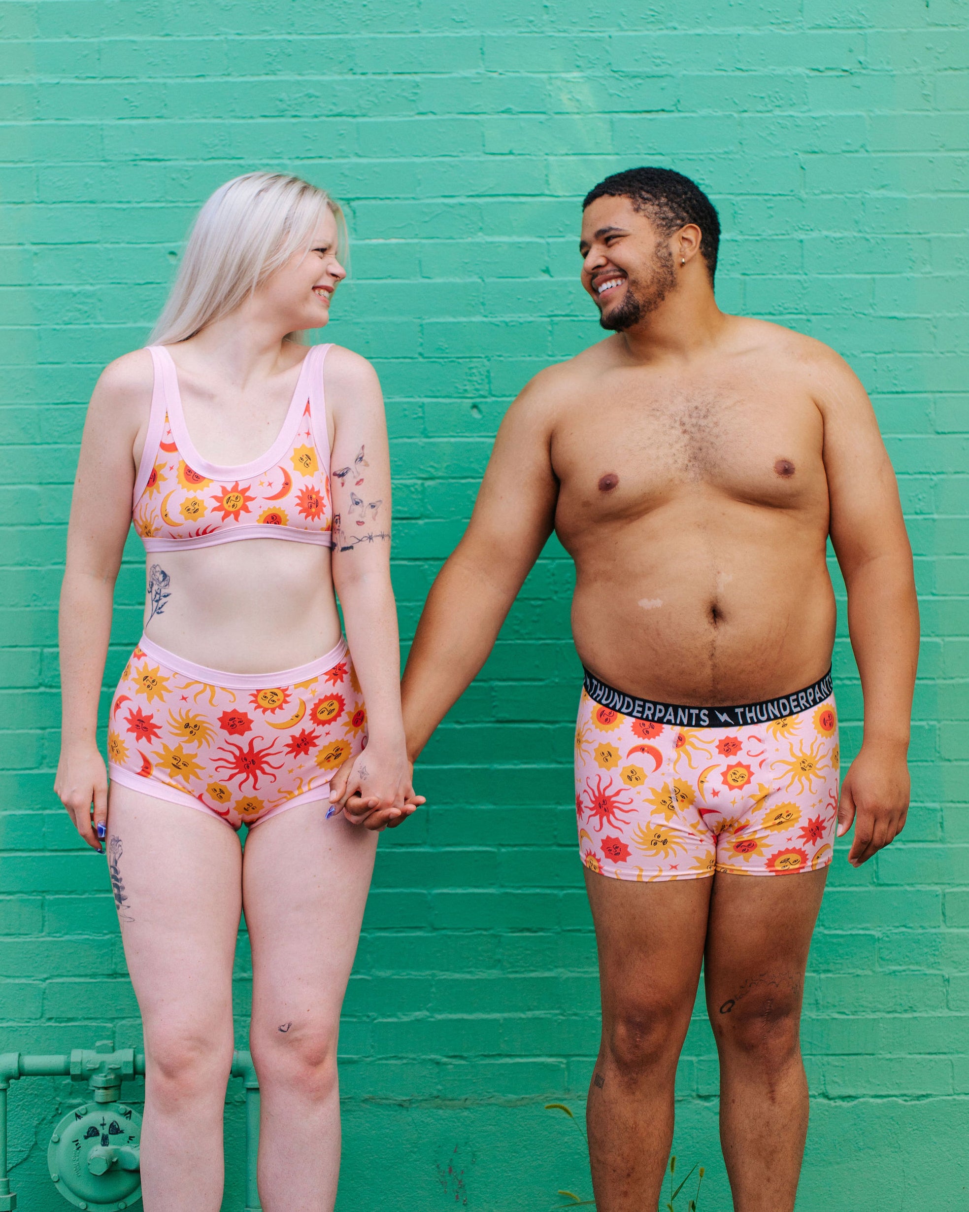 Two models wearing Thunderpants Sky Rise style underwear and Boxer Brief style underwear in Luna y Sol print - pink, yellow, and orange suns and moons.