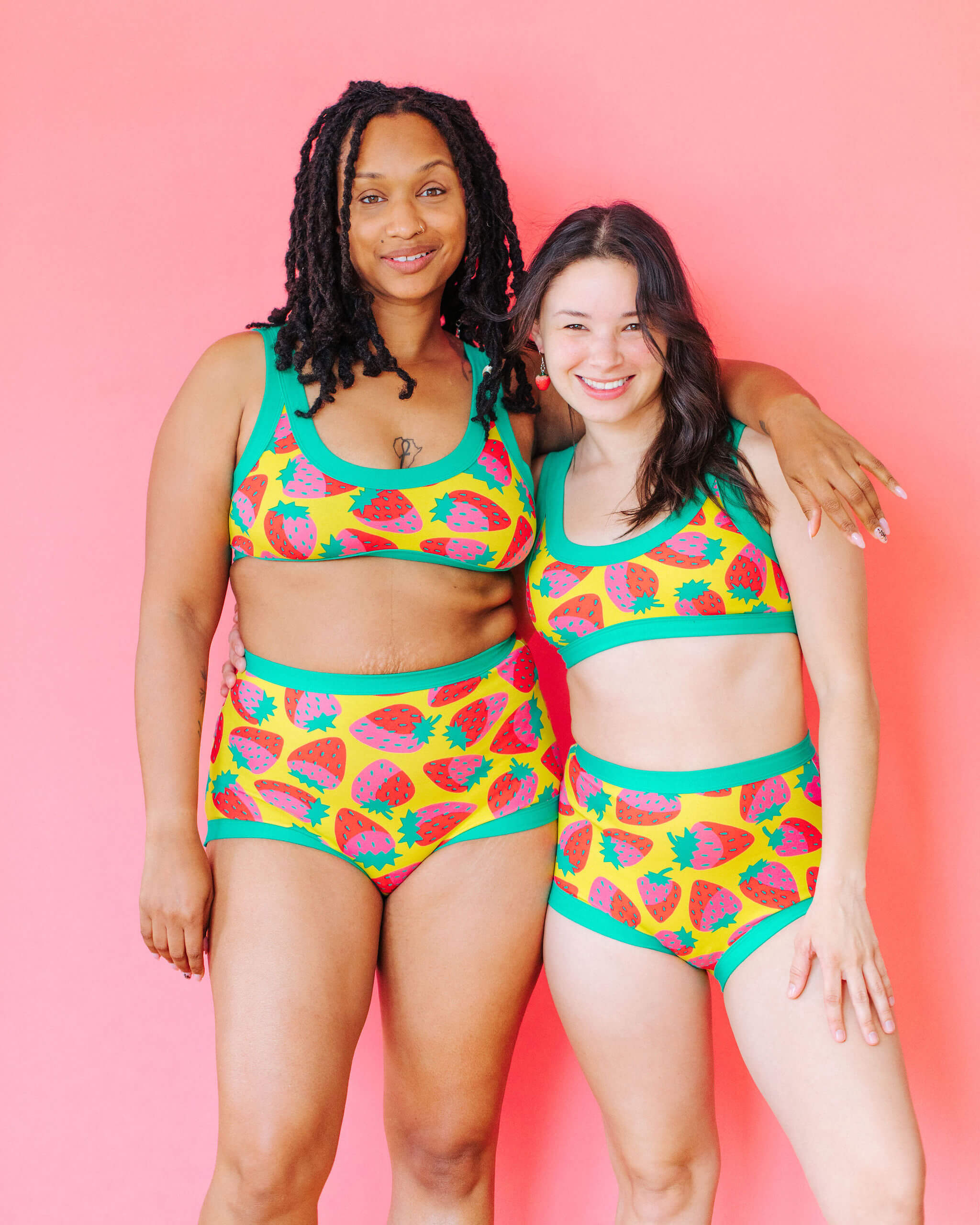 Models wearing Thunderpants Sky Rise style underwear and Bralette in a Strawberry print - pink, red, and peacock green on chartreuse. 