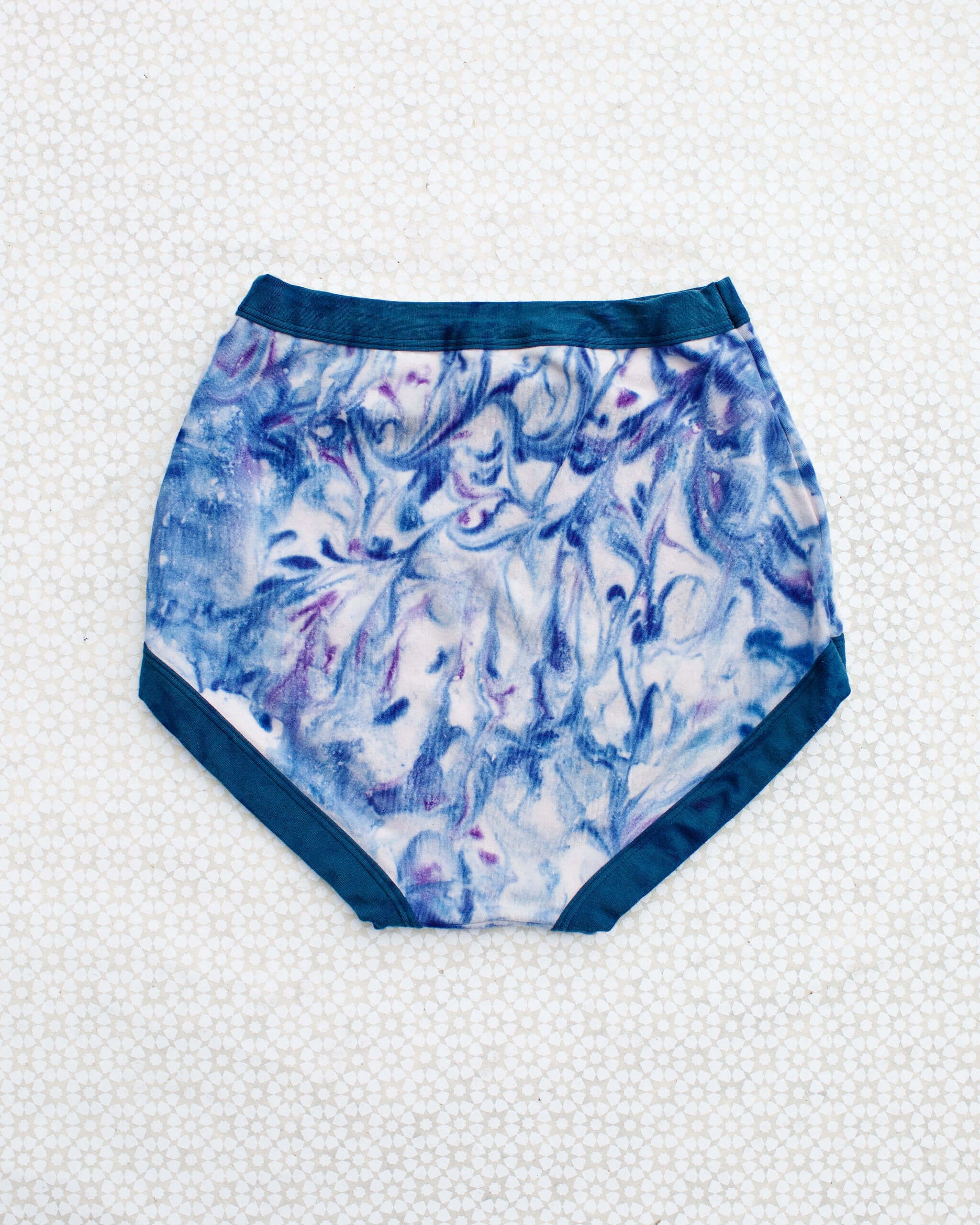 Flat lay of Thunderpants Sky Rise style underwear in Winter Blues Marble dye - different blues and purples swirled to look like marble. 