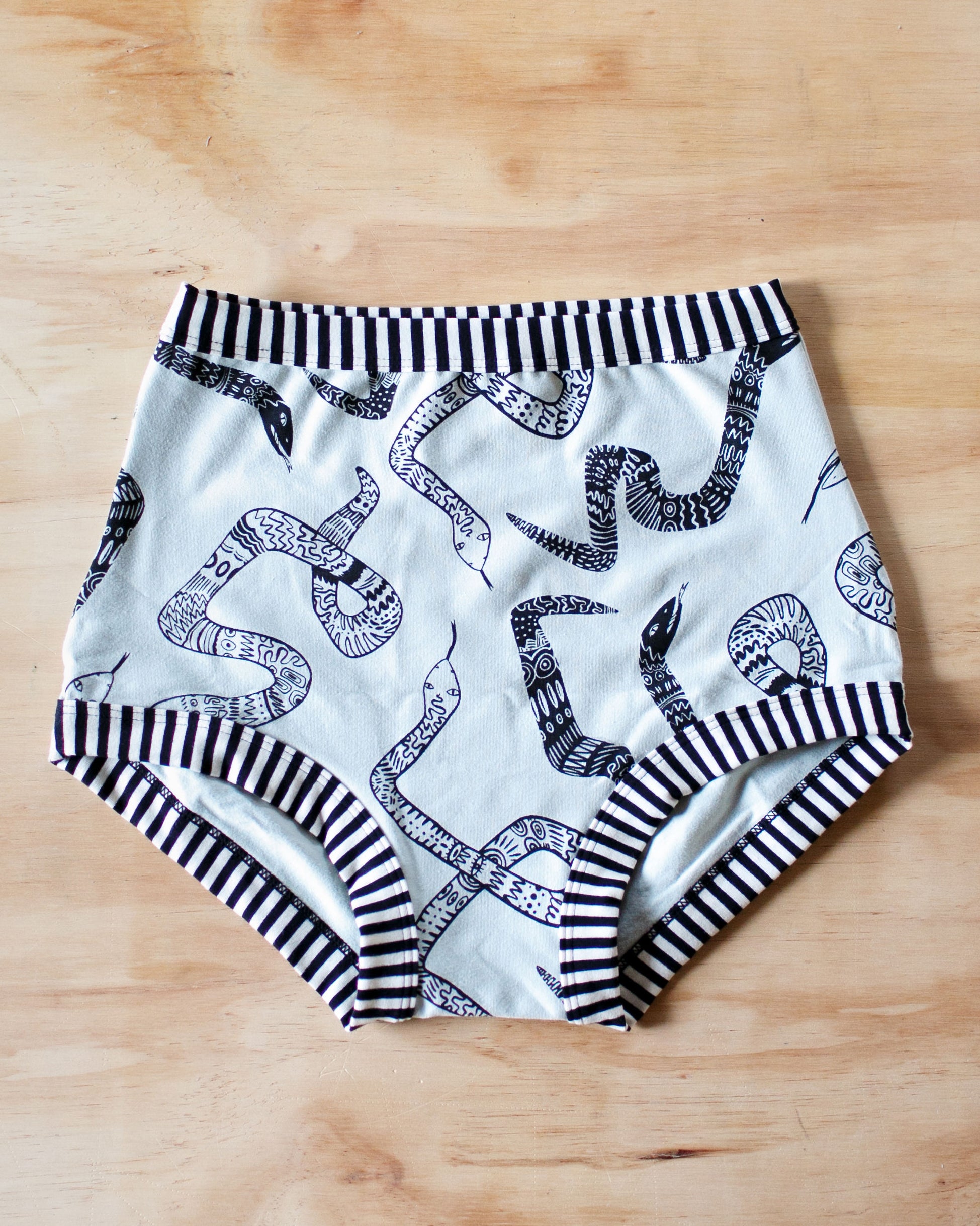 Flat lay of Thunderpants organic cotton Sky Rise style underwear in Sketchy Snakes: sage color with black sketched snakes and black and white stripe binding.