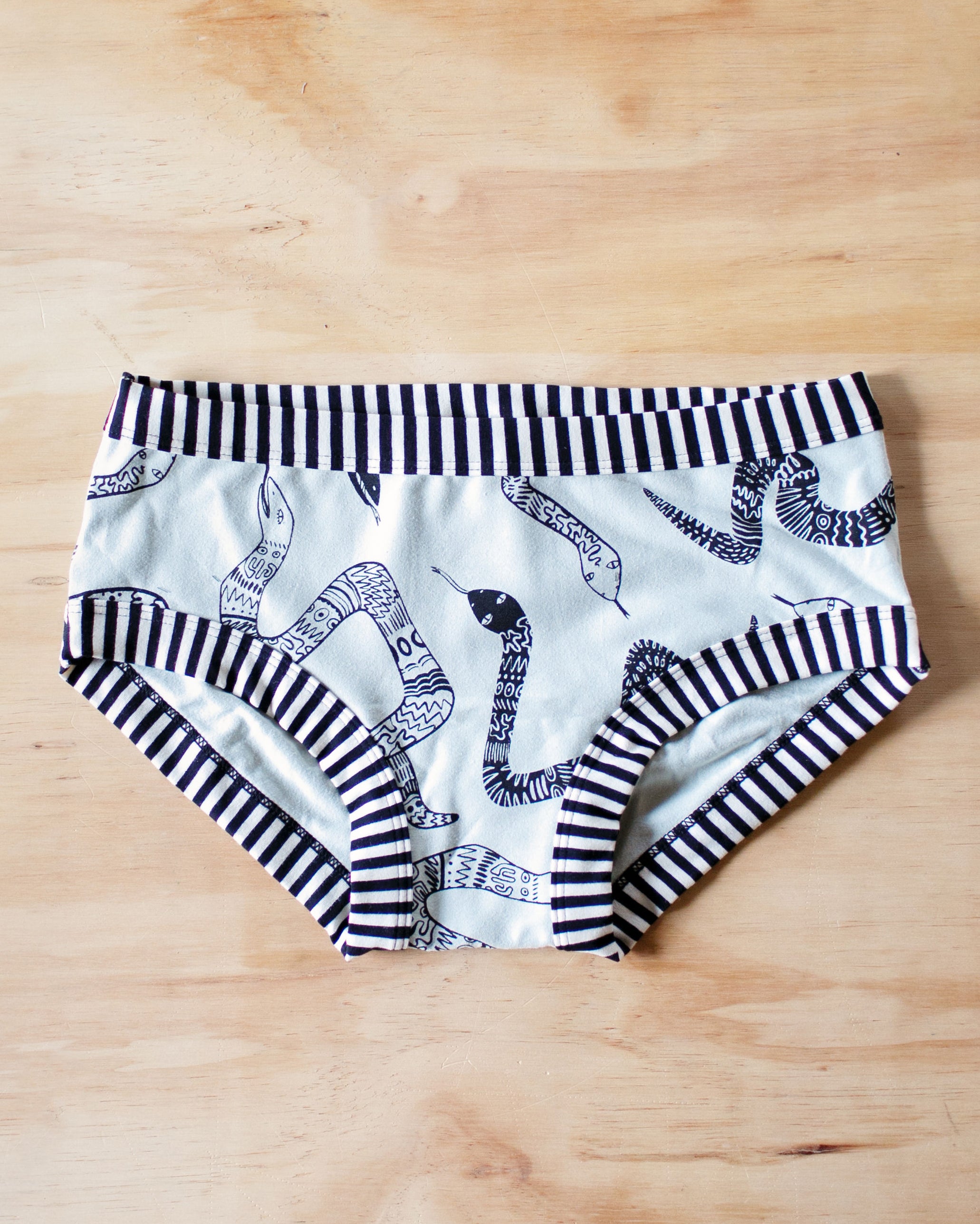 Flat lay of Thunderpants organic cotton Hipster style underwear in Sketchy Snakes: sage color with black sketched snakes and black and white stripe binding.