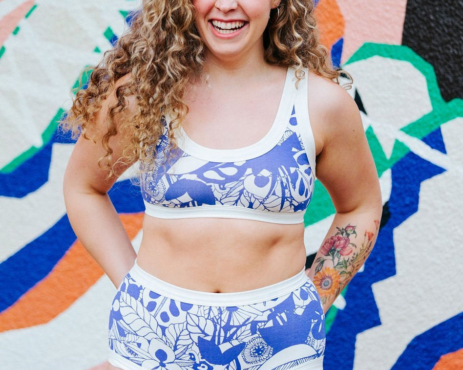 Laughing woman wearing Thunderpants organic cotton Original style underwear and Bralette in a blue jungle and floral print with a colorful background.