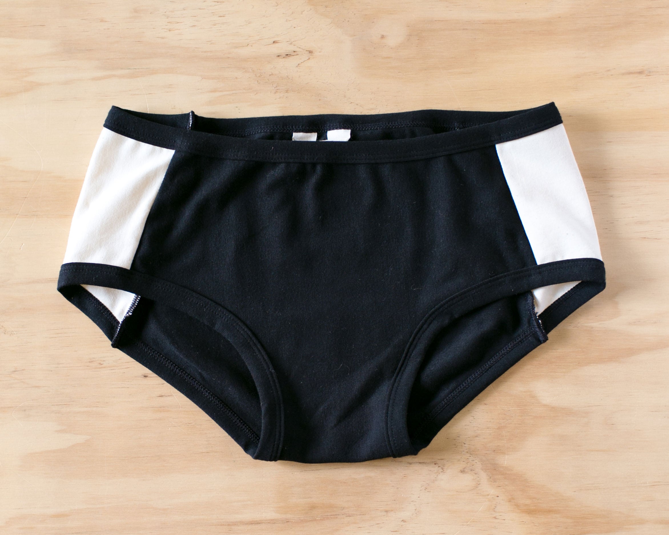 Flat lay on wood of our Cookies and Cream Panel Pants in the Hipster style: black panel in the center and vanilla panels on both sides with black binding.