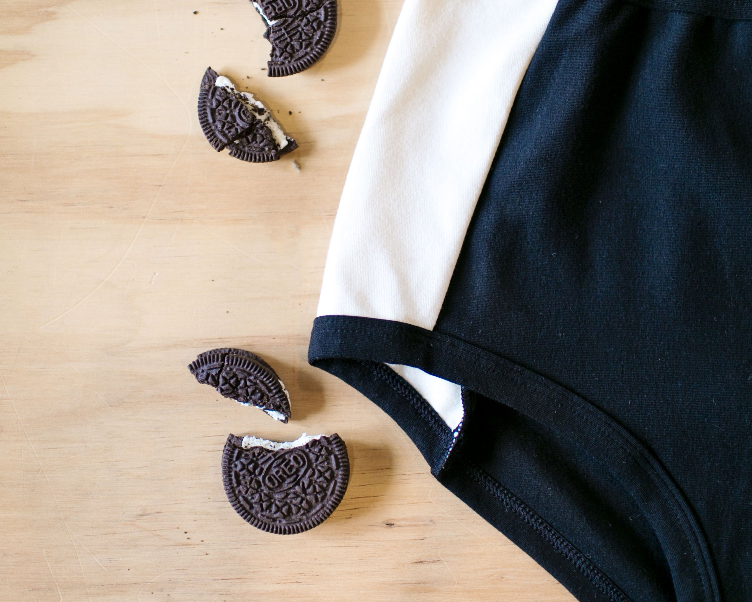 Close up flat lay on wood of our Cookies and Cream Panel Pants in the Original style with Oreo Cookies: black panel in the center and vanilla panels on both sides with black binding.