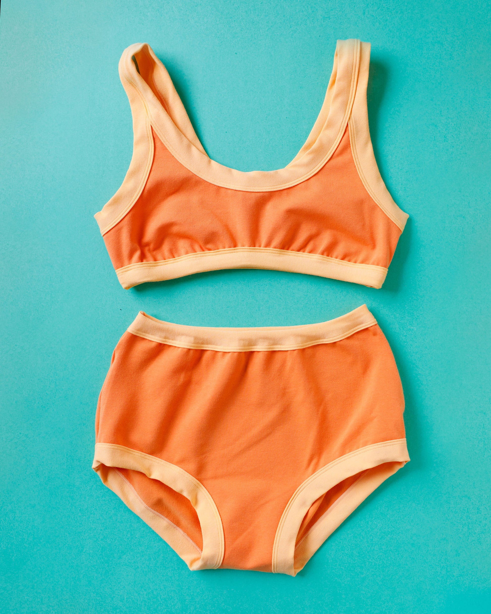 Flat lay of Thunderpants Bralette and Original style underwear in Creamsicle: dark orange with light orange binding.