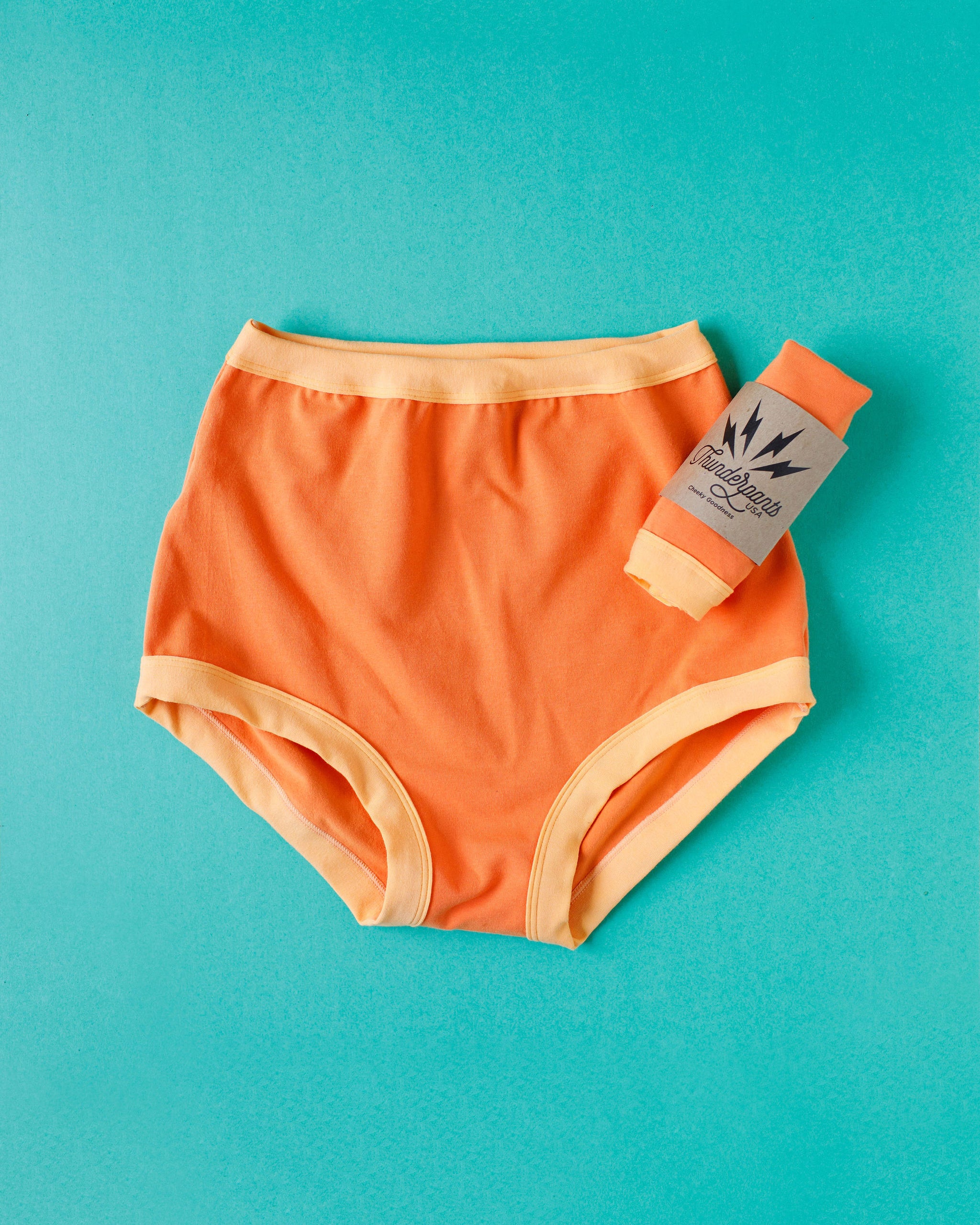 Flat lay of Thunderpants Sky Rise style underwear in Creamsicle: dark orange with light orange binding.