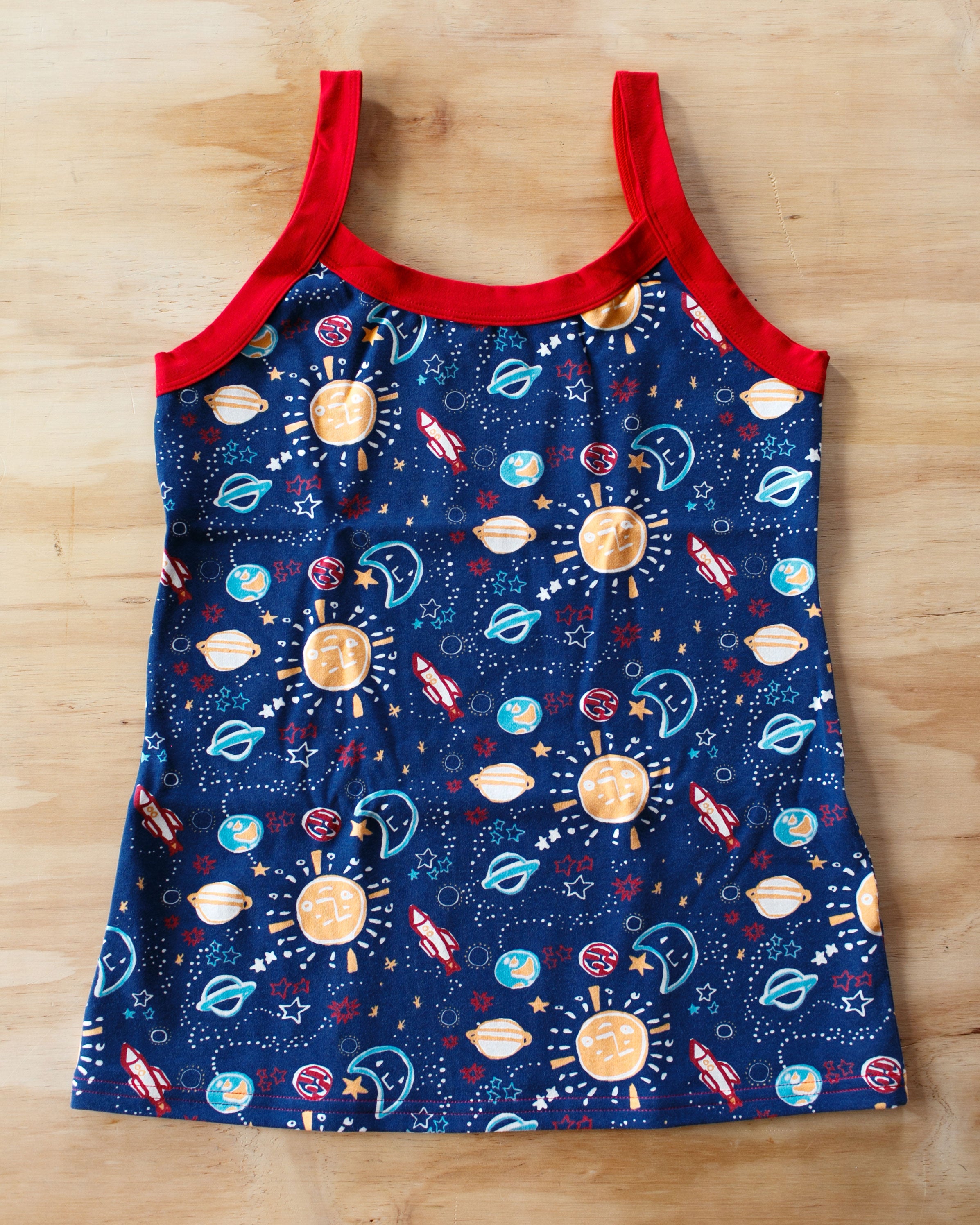 Flat lay of Thunderpants organic cotton Camisole in sun, planets, stars, and universe print with red binding.