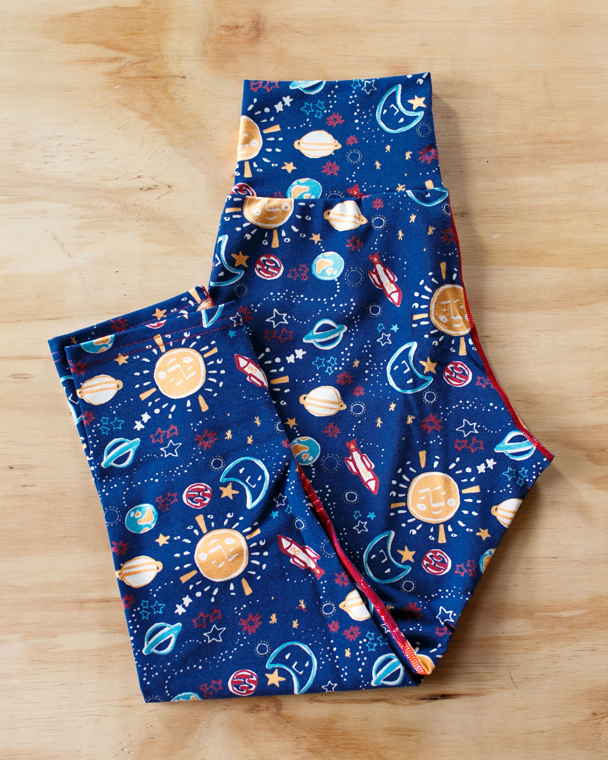 Flat-lay of Thunderpants organic cotton 3/4 leggings in our Dark Sky print: colorful drawings of the universe.