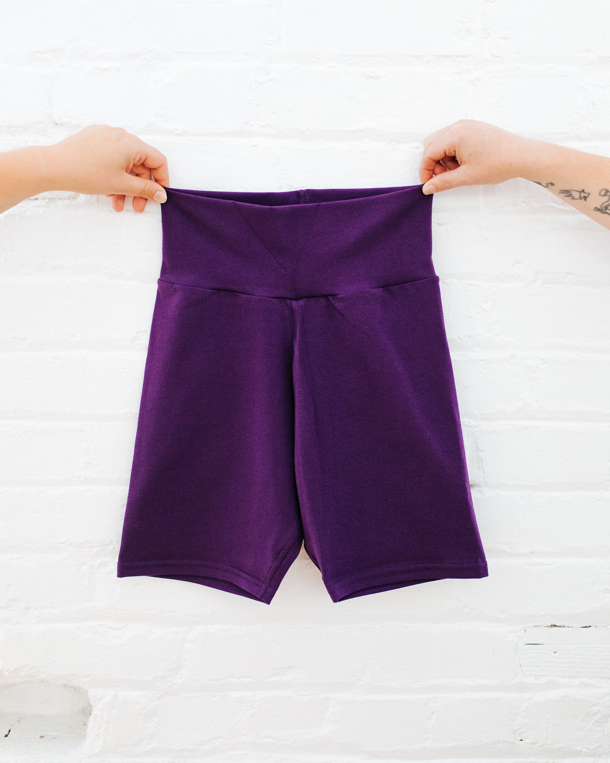 Purple Deep Amethyst Bike Shorts being held up against a white brick background.