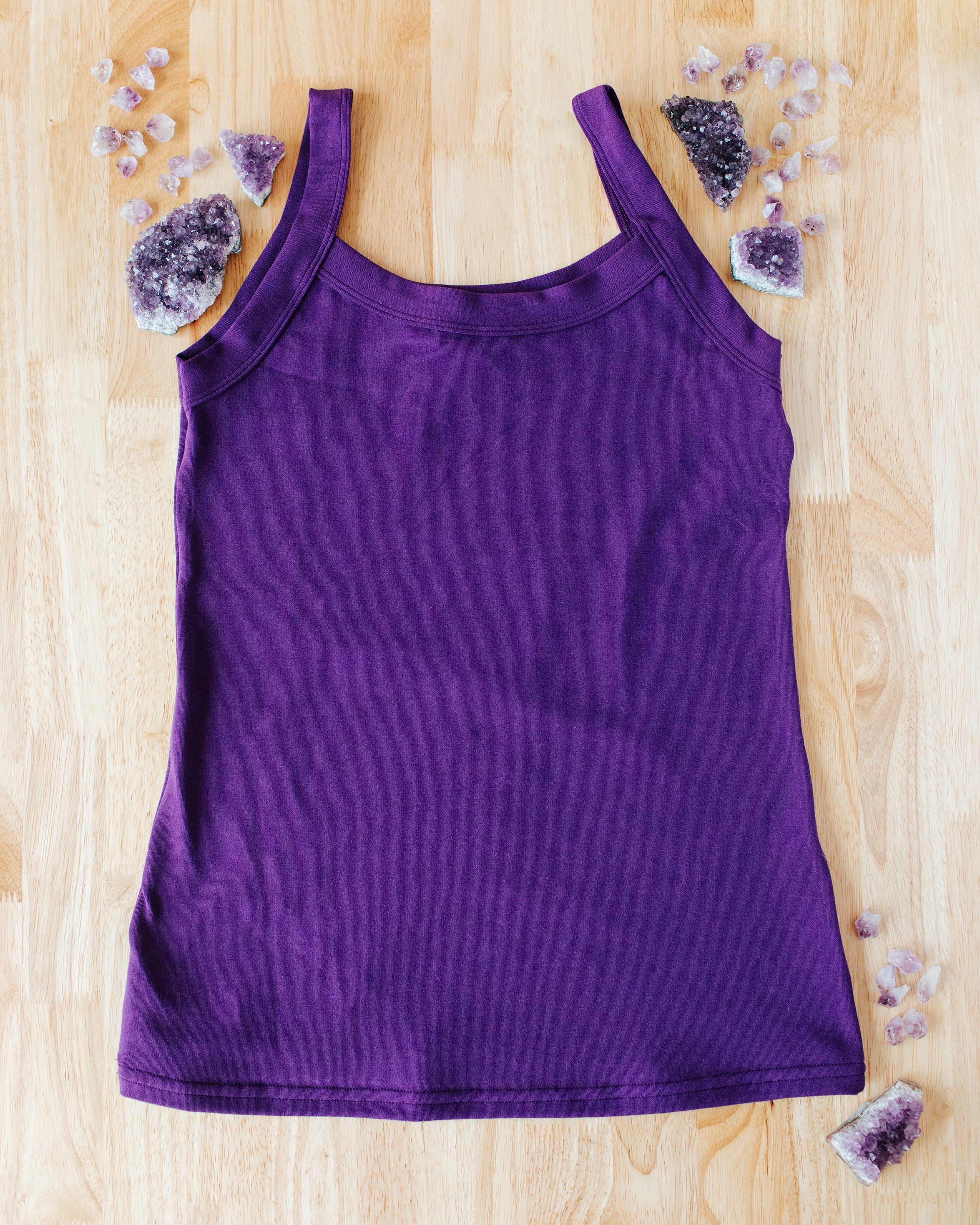 Flat lay of purple Deep Amethyst Camisole on a wood surface with big and small amethyst stones surrounding it.