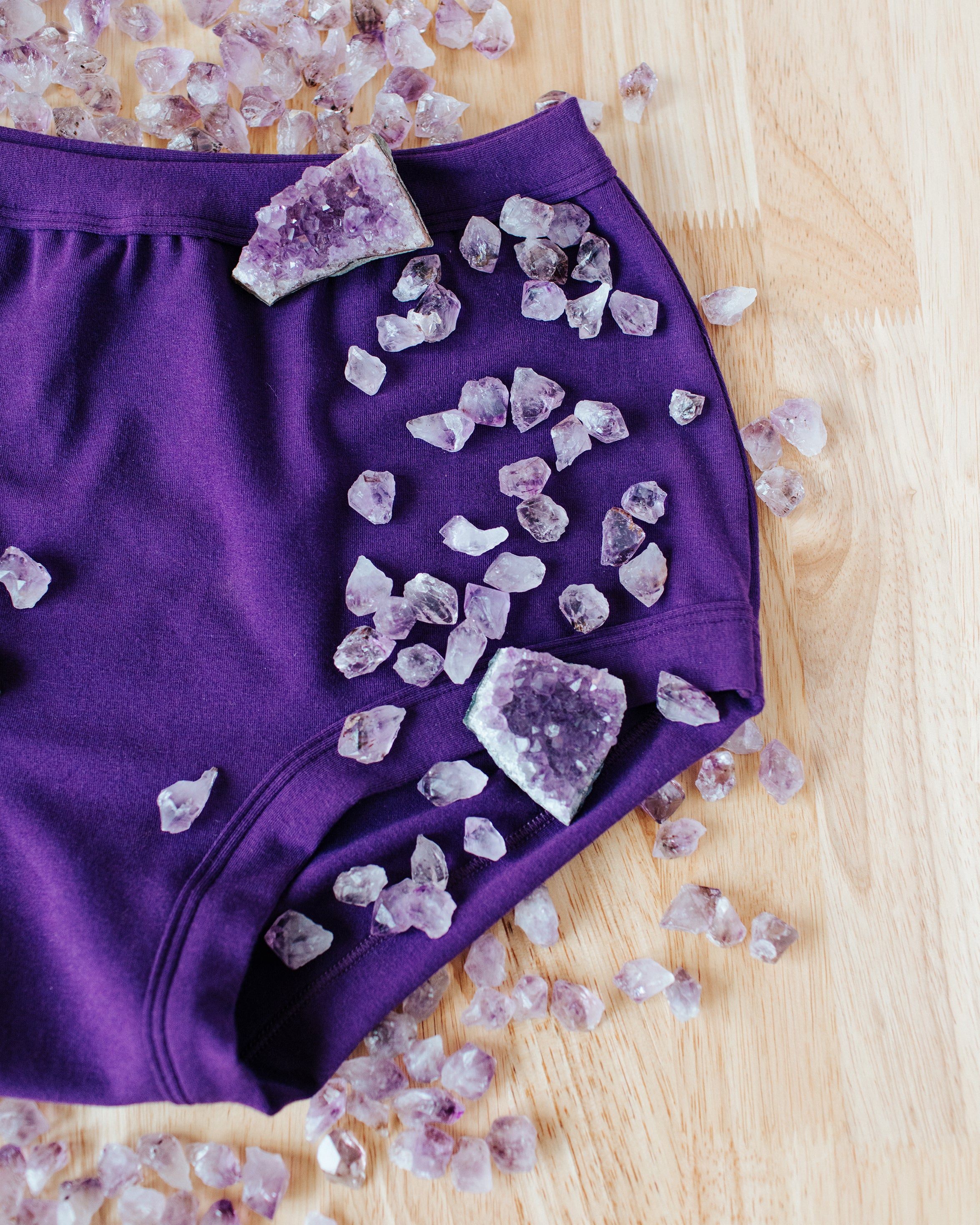 Close up flat lay of purple Deep Amethyst on a wood surface with large and small amethyst stones on and around it.