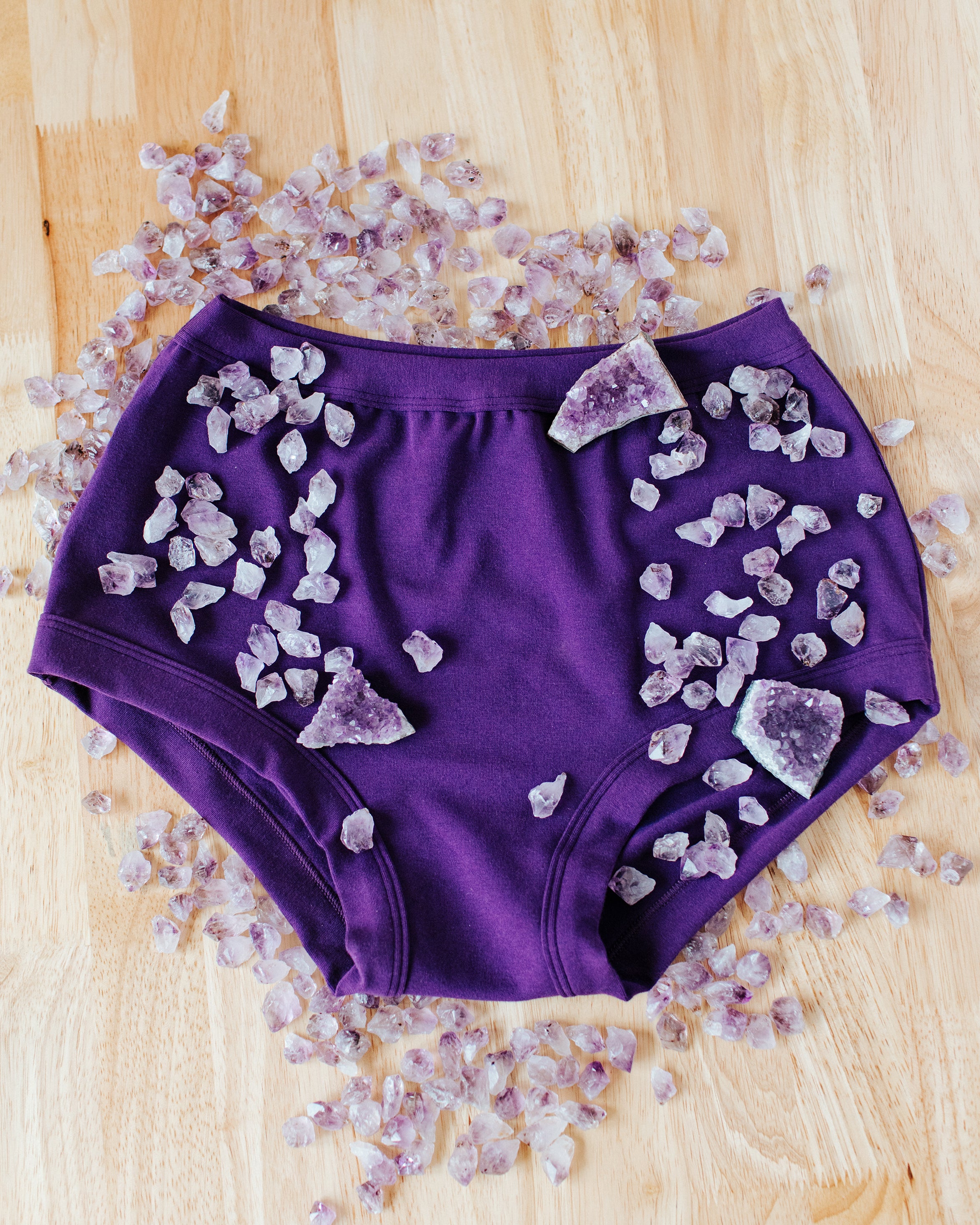 Flat lay of purple Deep Amethyst Original style underwear with large and small amethysts stones on and surrounding it.