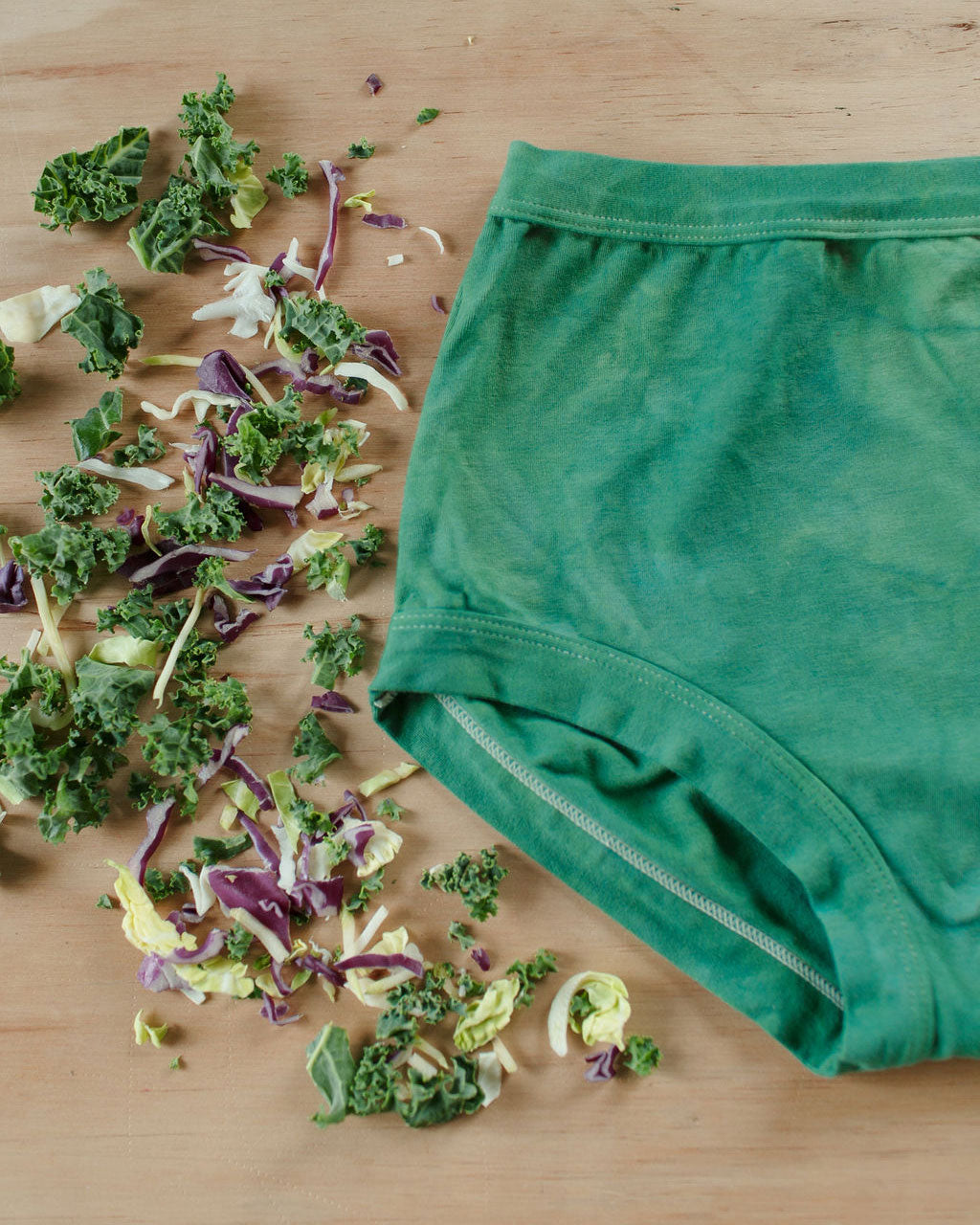 Flat lay of Thunderpants organic cotton Original style underwear in hand dye Emerald with kale around.