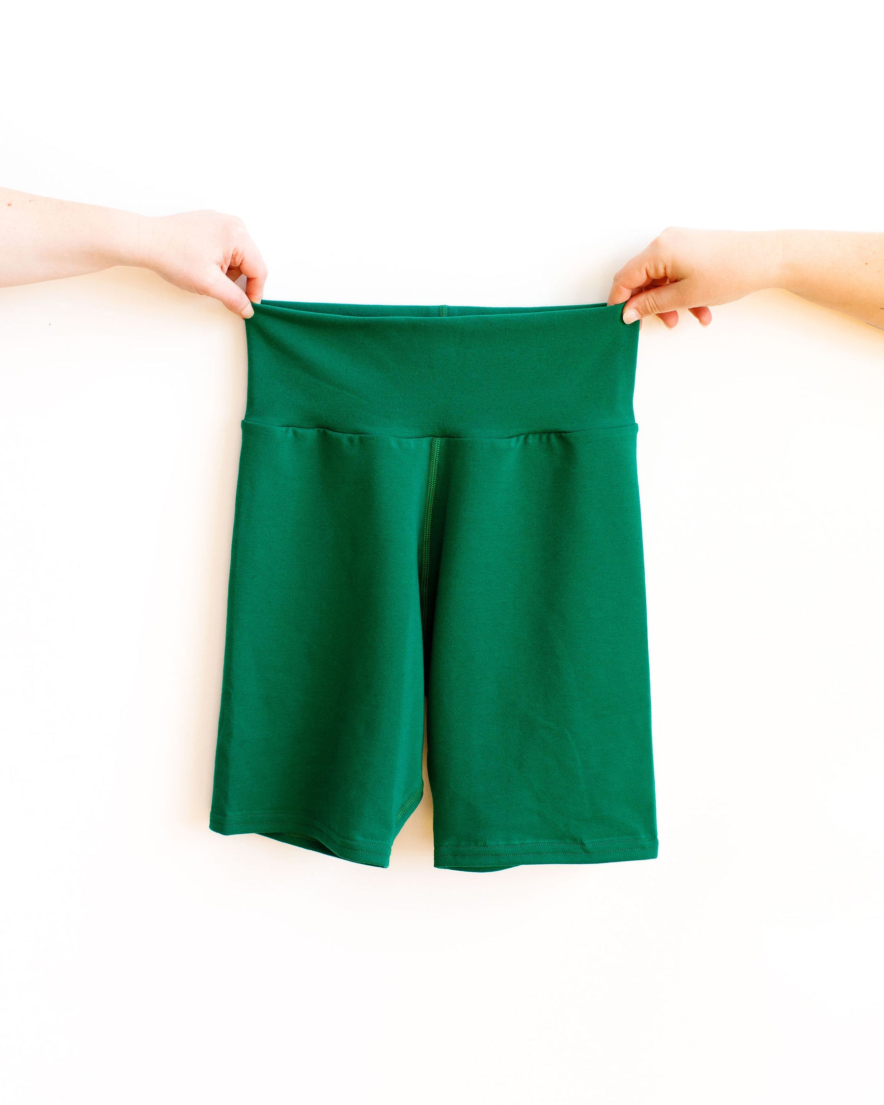 Two hands holding Emerald Green Thunderpants Bike Shorts against a white wall.