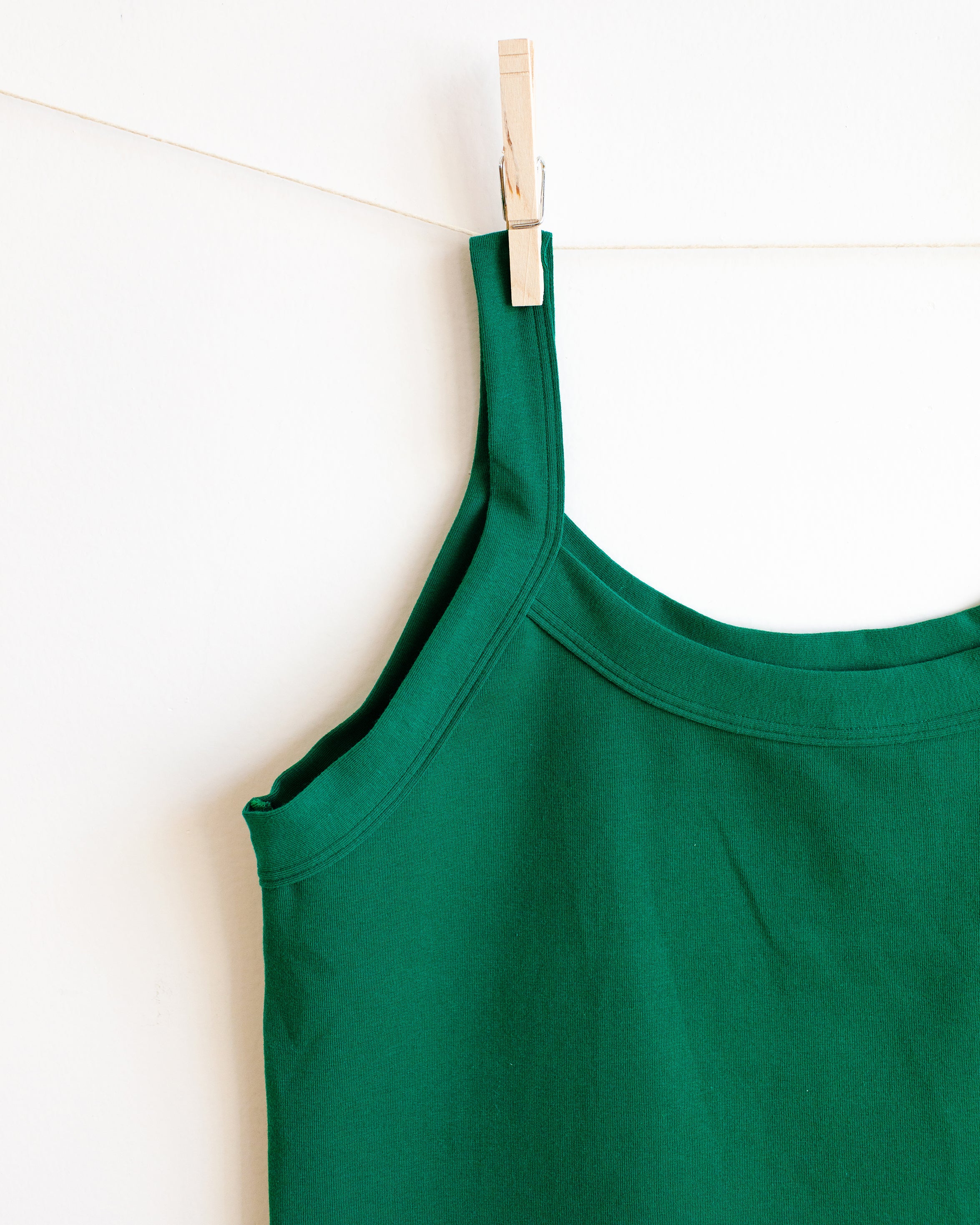 Close up of Thunderpants Camisole in Emerald Green hanging by a clothes pin on a white wall. 