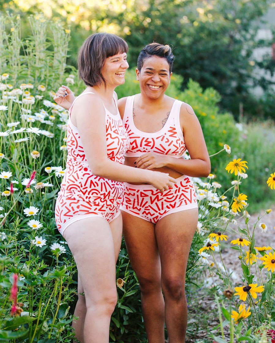 Models standing together laughing outside wearing Thunderpants organic cotton Hipster style underwear, Camisole, Bralette, and Original style underwear in our Energy Vibes print: Perfect Pink with dark pink large squiggles.
