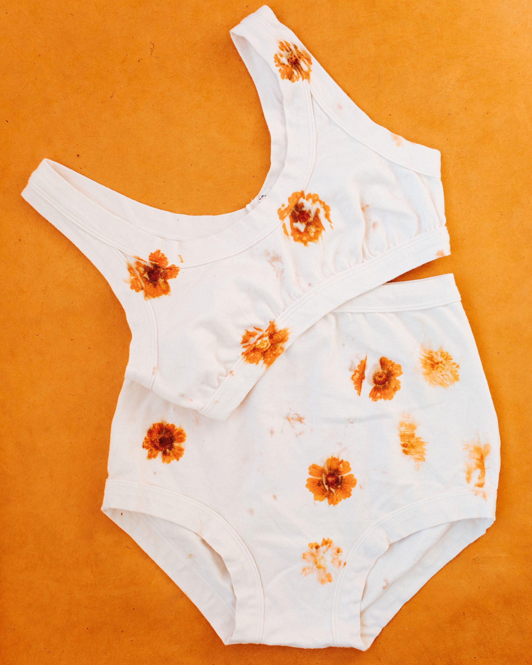 Flat lay on an orange surface of Thunderpants Sky Rise style underwear and Bralette in the Limited Edition Flower Press Botanical Dye - flowers pressed on the underwear to create a print.