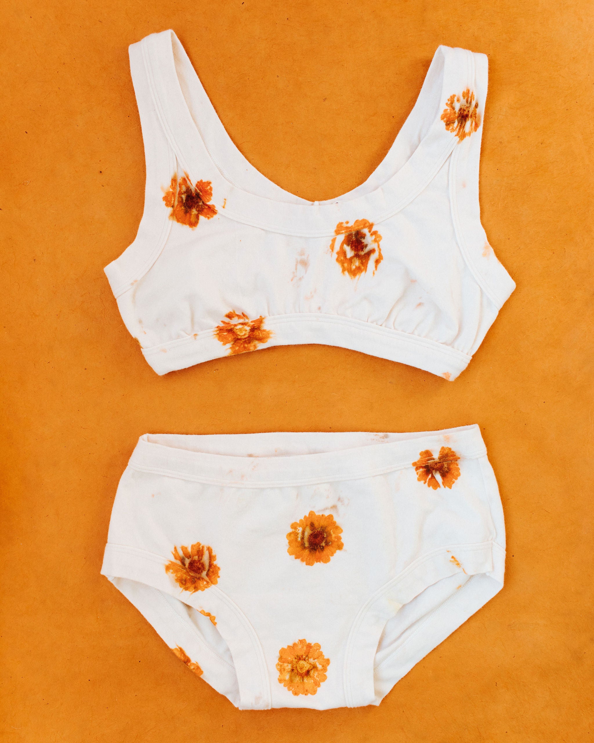 Flat lay on an orange surface of Thunderpants Hipster style underwear and Bralette in the Limited Edition Flower Press Botanical Dye - flowers pressed onto the fabric to create a print.